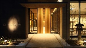 Une entrée d’hôtel moderne avec une façade en bois, des portes en verre et un chemin pavé menant à l’entrée.