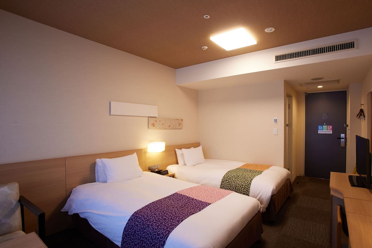 A hotel room with two beds, a desk, a chair, and a nightstand.