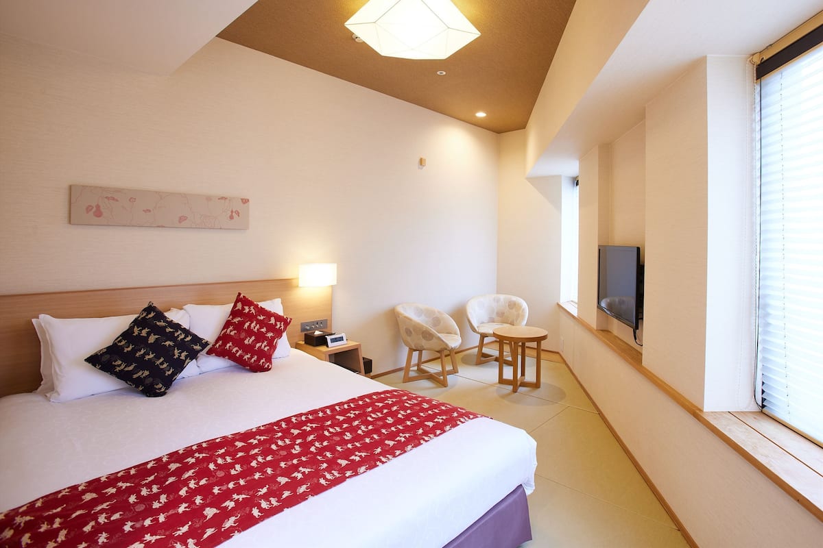 A hotel room with a large bed, a TV, a desk, and a chair.