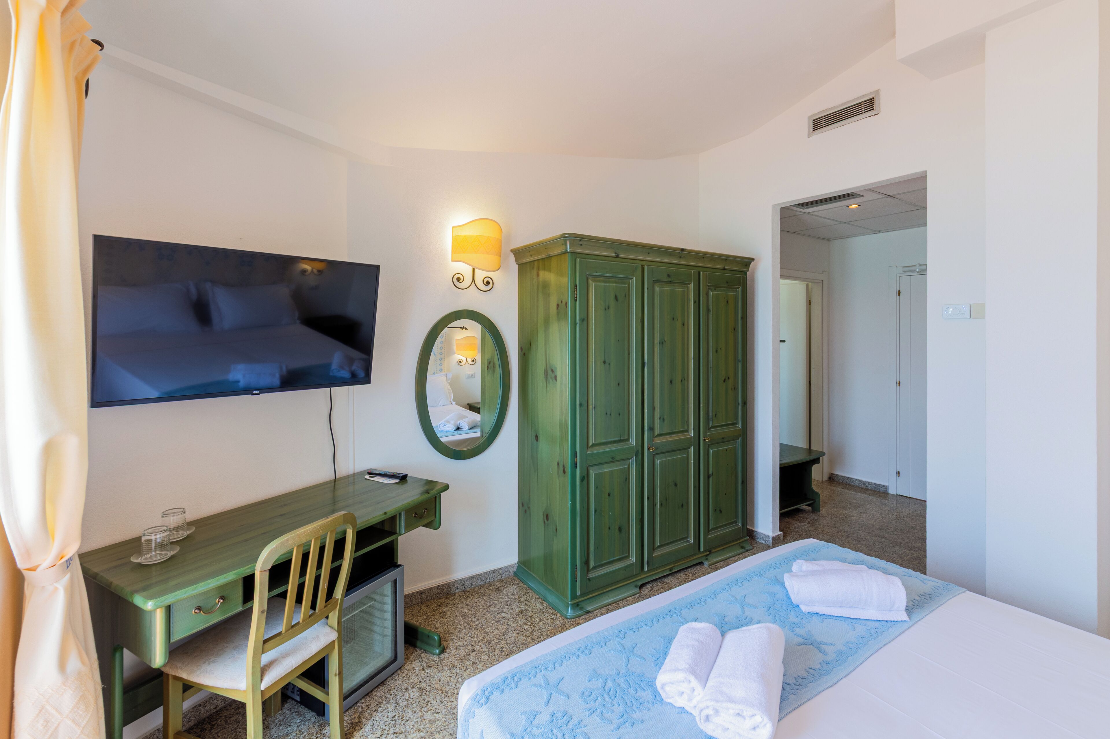 A hotel room with a bed, a desk, a chair, a television, a wardrobe, and a mirror.
