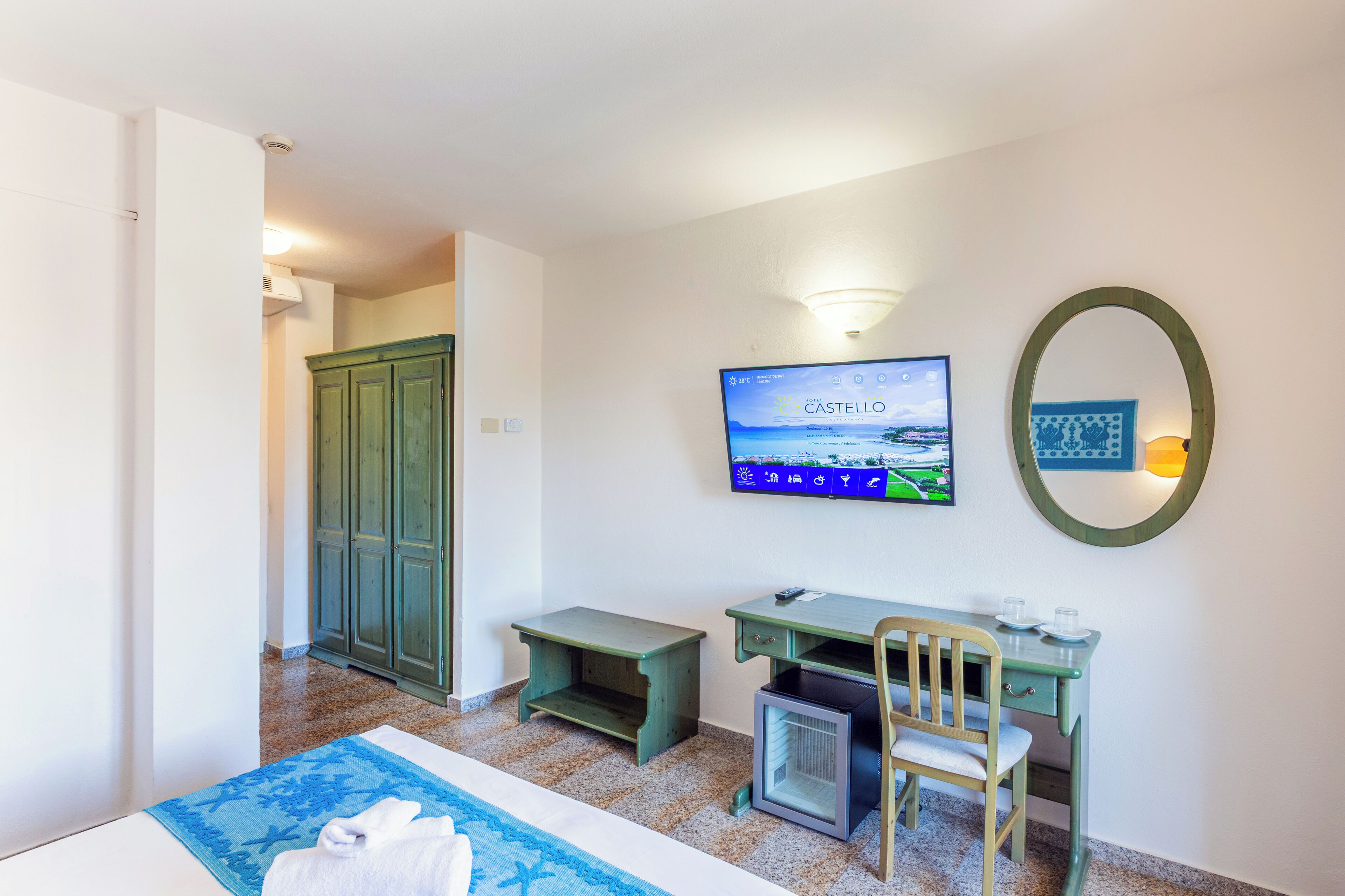 A hotel room with a bed, a desk, a chair, a television, and a wardrobe.