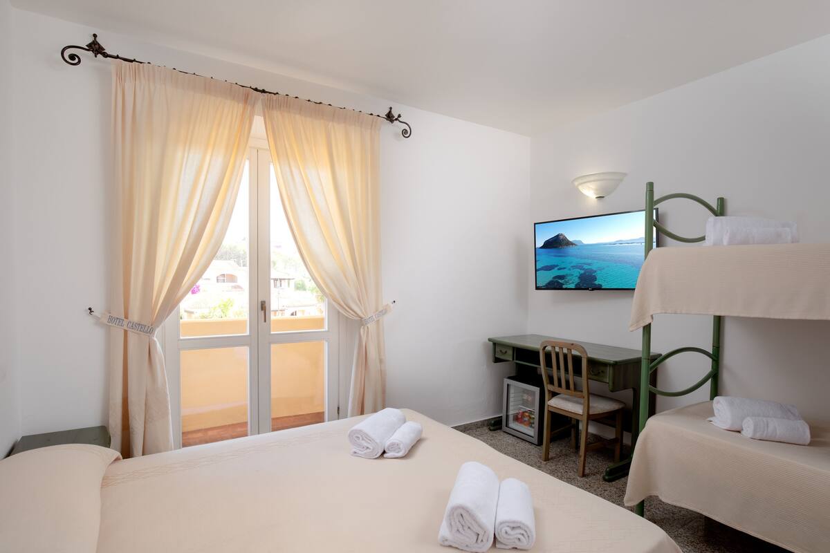 Una habitación de hotel con una cama, un escritorio, una silla, un televisor y una litera.