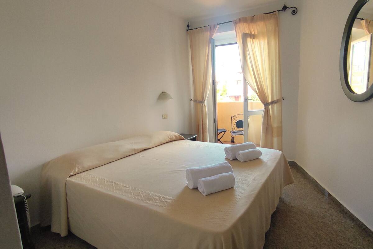 Habitación de hotel con cama, una silla, una mesa y ventana con cortinas.