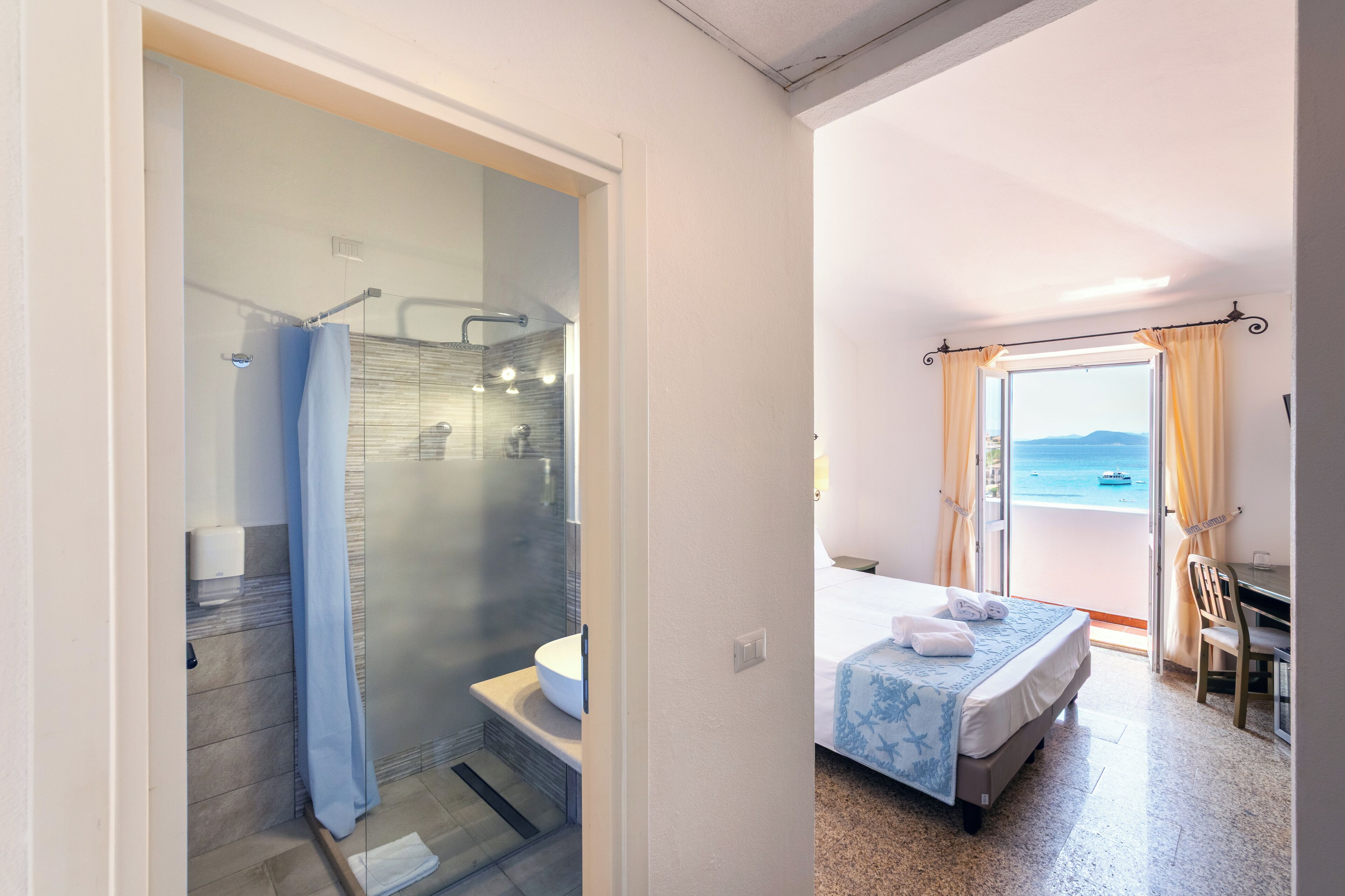 Hotelkamer met badkamer, voorzien van een douchecabine met glazen wanden en een balkon met uitzicht op zee.
