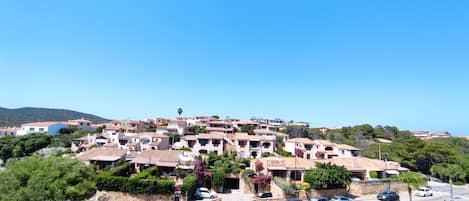 A hillside residential area with terraced houses, a road with cars, and a clear blue sky.