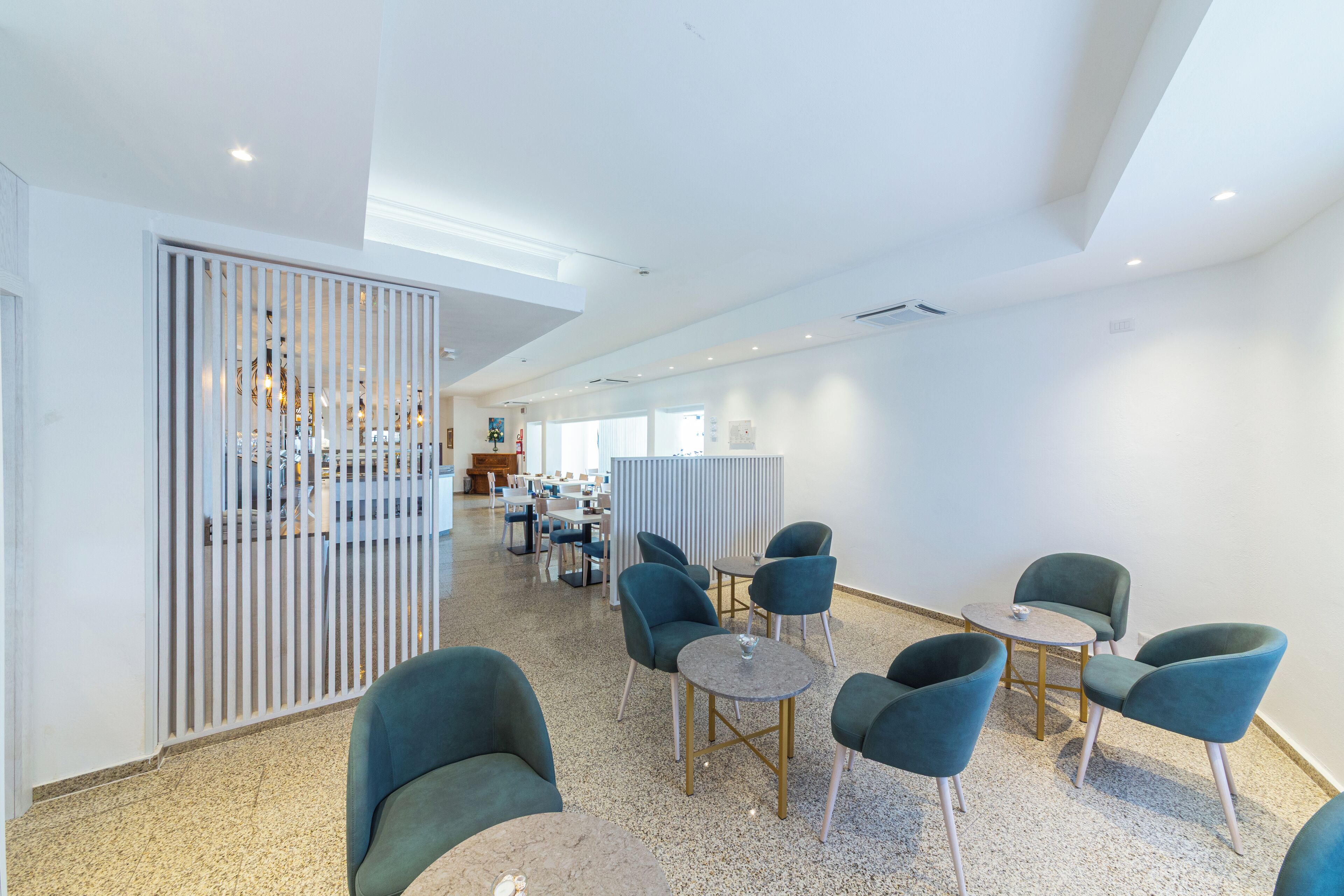 Een moderne hotellobby met een hoge plafond, een receptiebalie en zithoeken met ronde tafels en stoelen.