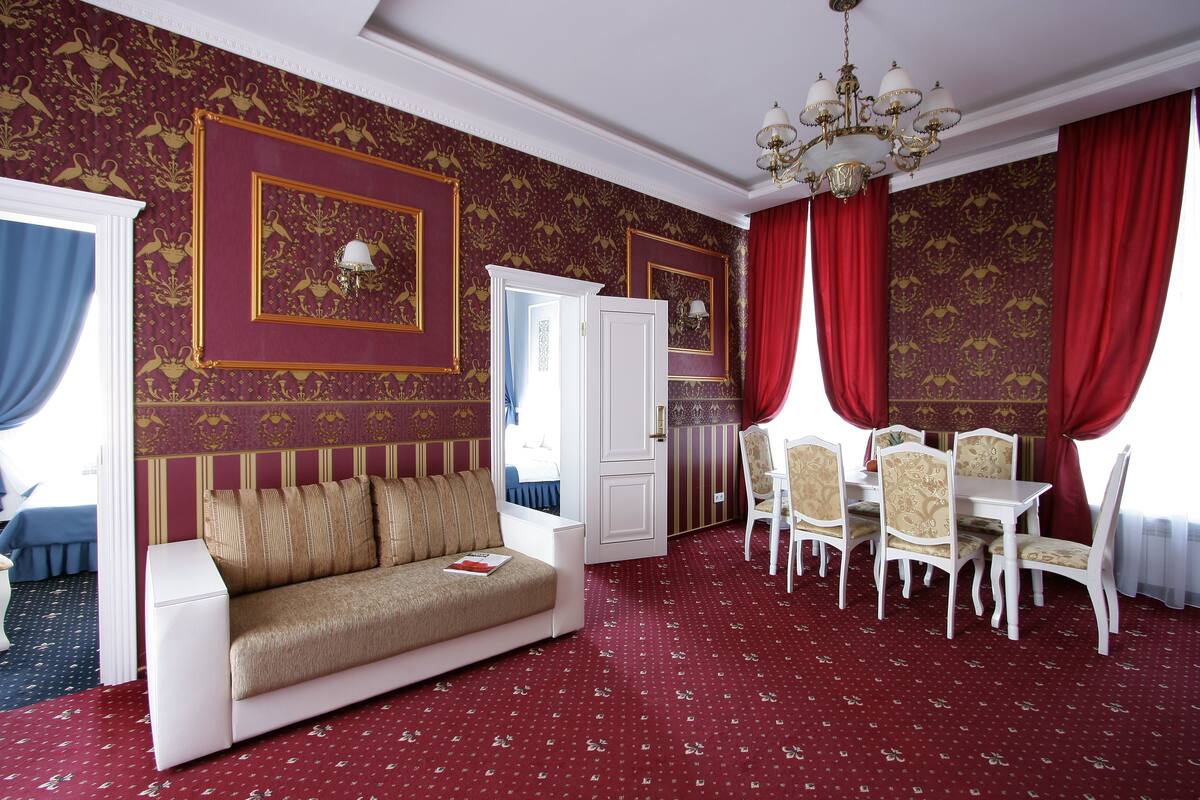 A hotel room with a red carpet, a sofa, a dining table with chairs, and a chandelier.
