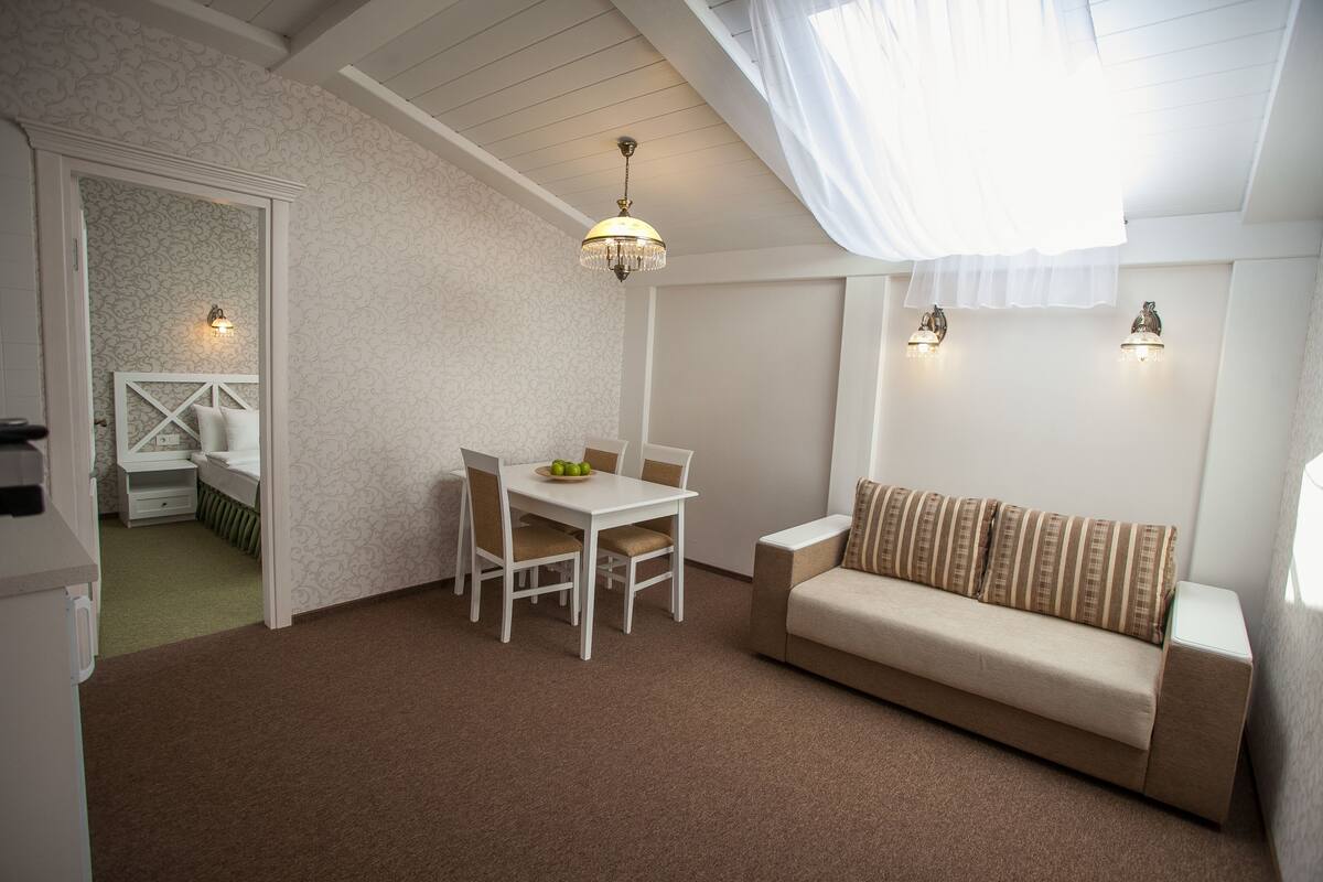 A cozy room with a white ceiling, a dining table with chairs, a sofa, and two wall-mounted lights.