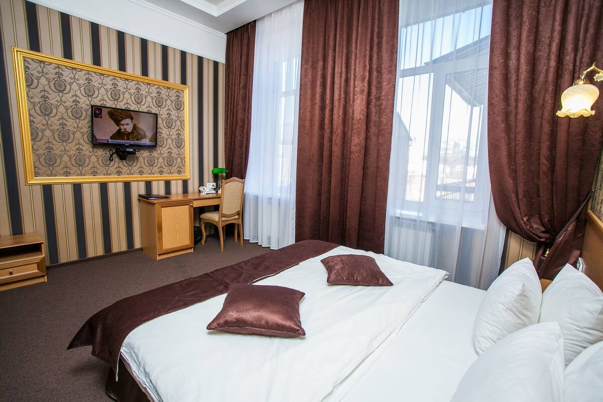 A hotel room with a large bed, a desk, a television, and curtains.