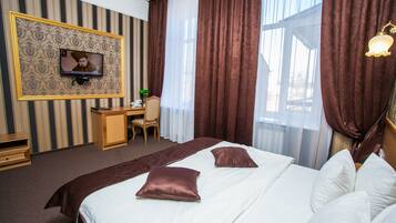 Habitación de hotel con una cama grande, un escritorio, un televisor y cortinas.