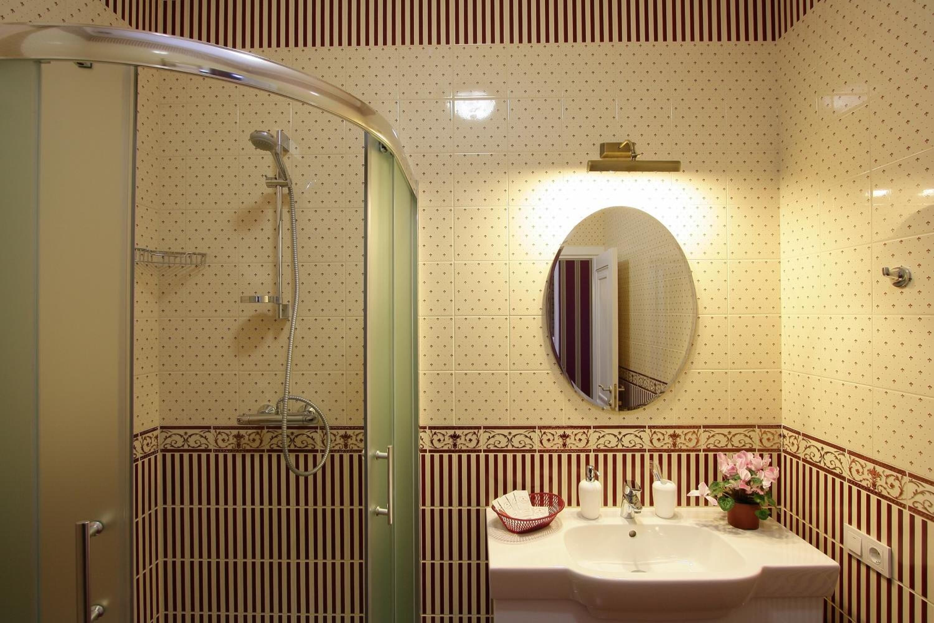 Un baño con ducha de vidrio, lavamanos con espejo y azulejos decorativos.