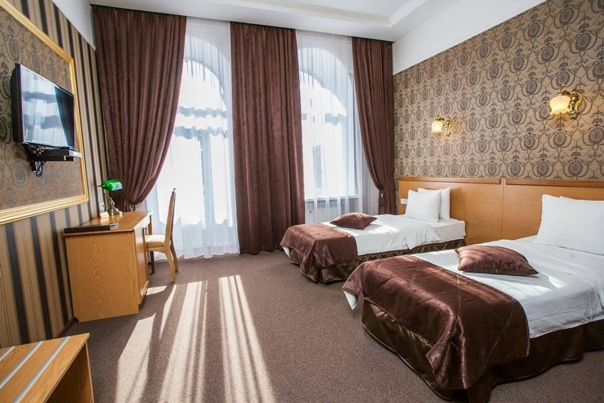 A hotel room with two beds, a desk, a chair, and a TV.
