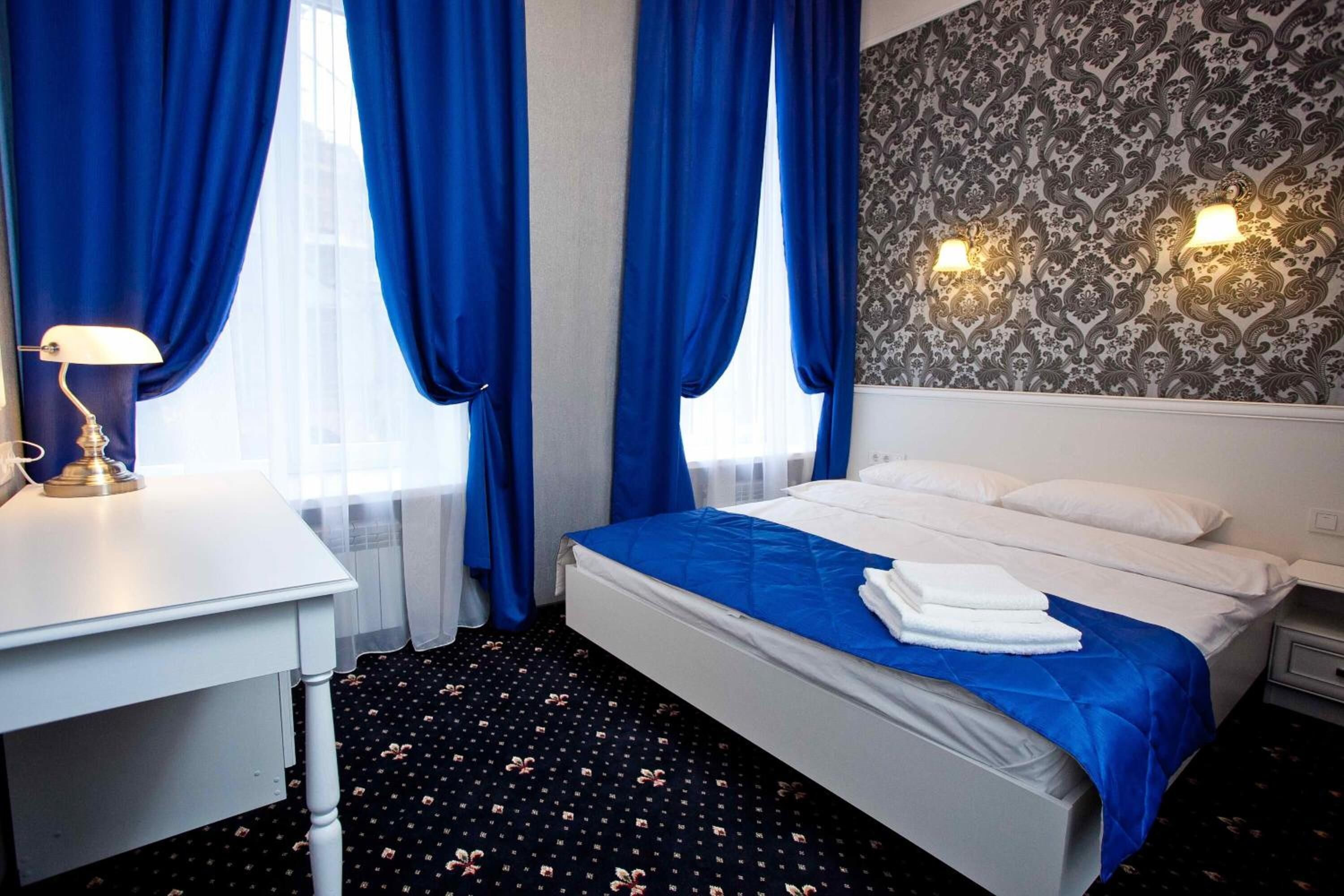 A hotel room with a bed, a desk with a lamp, and a patterned wall.