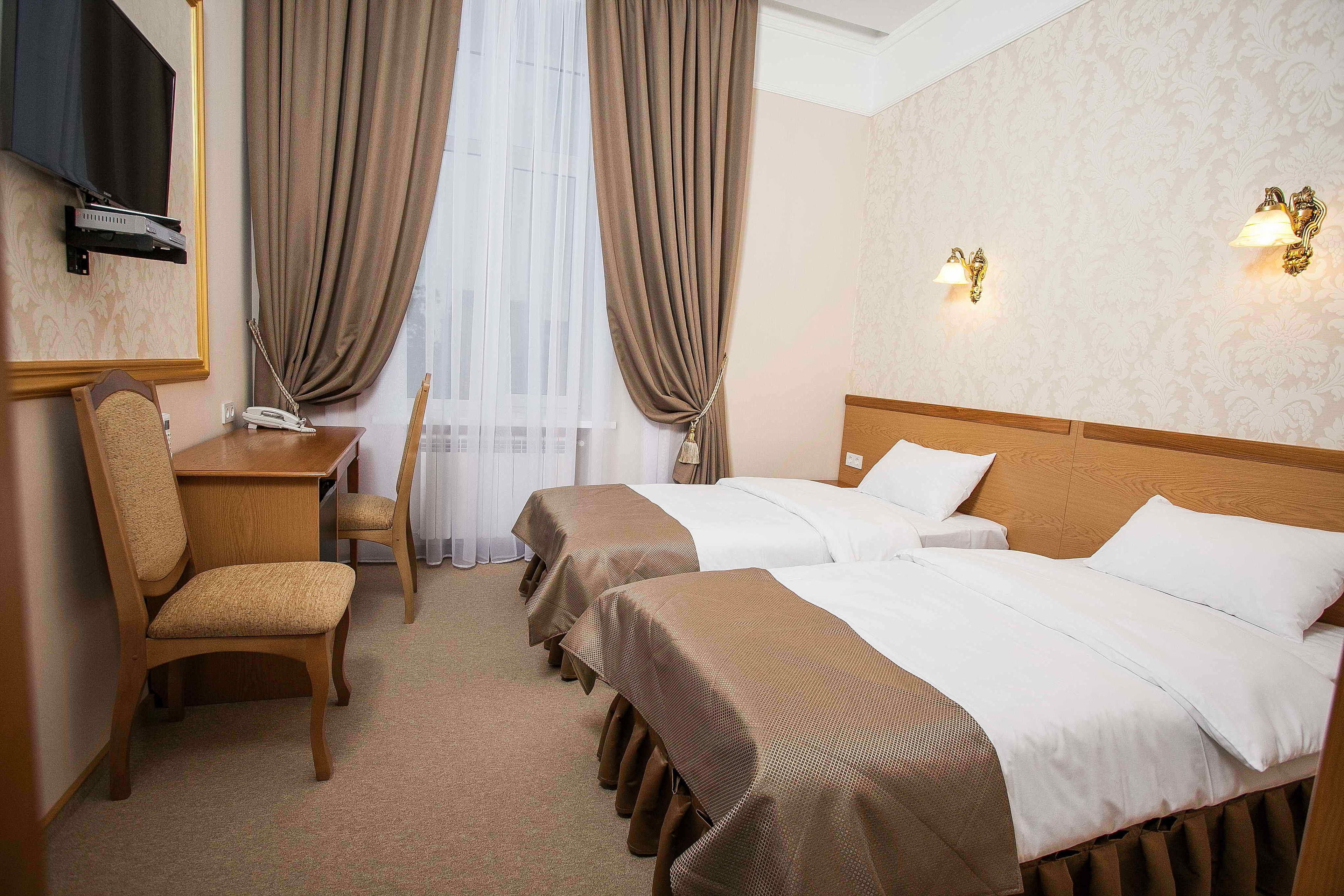 A hotel room with two beds, a desk, a chair, and a TV.