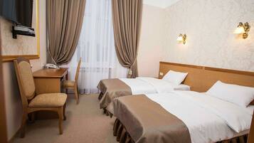 A hotel room with two beds, a desk, a chair, and a TV.