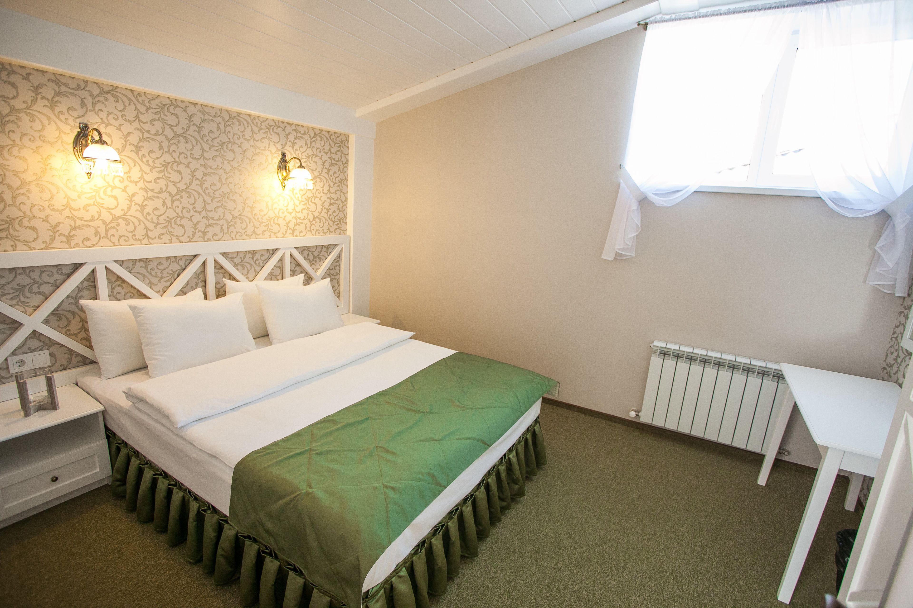A neatly arranged bedroom with a bed, bedside tables, a radiator, and a window with sheer curtains.