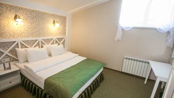 A neatly arranged bedroom with a bed, bedside tables, a radiator, and a window with sheer curtains.