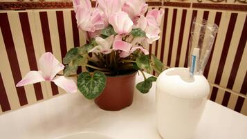 A bathroom with a white sink, a potted plant with pink flowers, and a white cup with a straw.