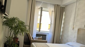 A hotel room with a large bed, a desk, a chair, a potted plant, and a TV mounted on the wall. - B&B Living (Rome)
