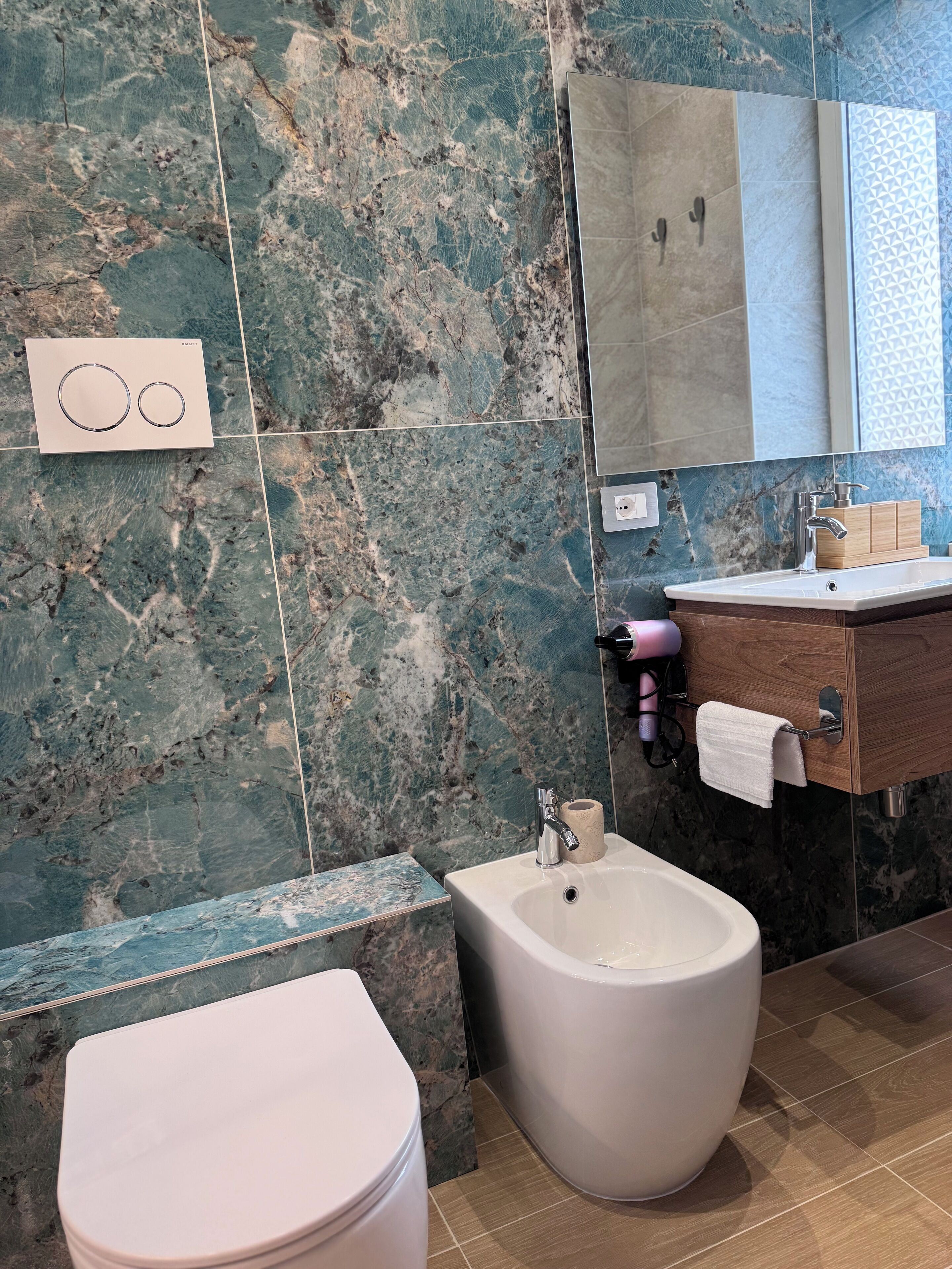 Un baño con bidé, inodoro, lavabo con espejo y un perchero para toallas.