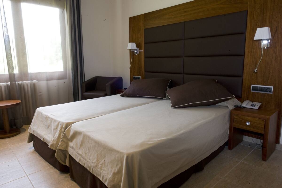 Ein Hotelzimmer mit zwei Betten, einem Holzkopfstück, Nachttischlampen, einem Telefon und einem kleinen Tisch.