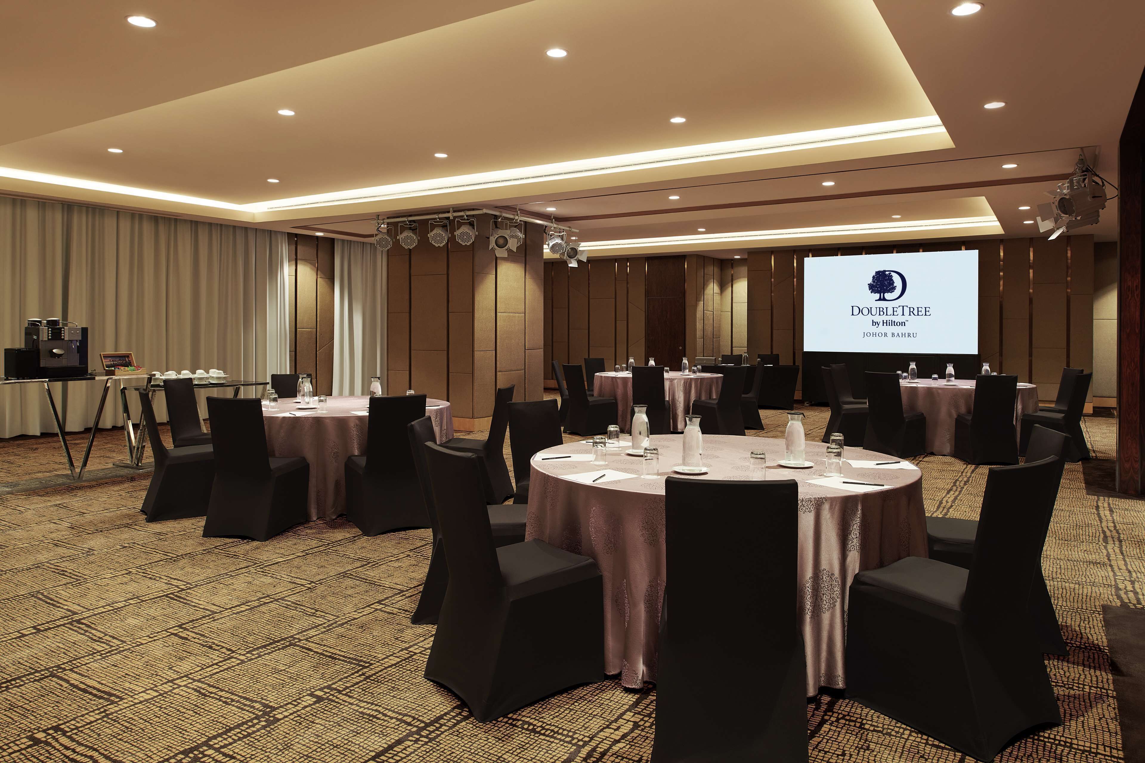 Un salón de conferencias con mesas redondas, sillas negras y una pantalla de proyección que muestra el logotipo de DoubleTree.