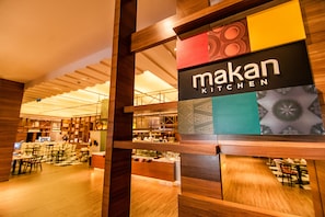 A restaurant interior with a wooden ceiling, tables, and chairs. A sign reads "Makan Kitchen".