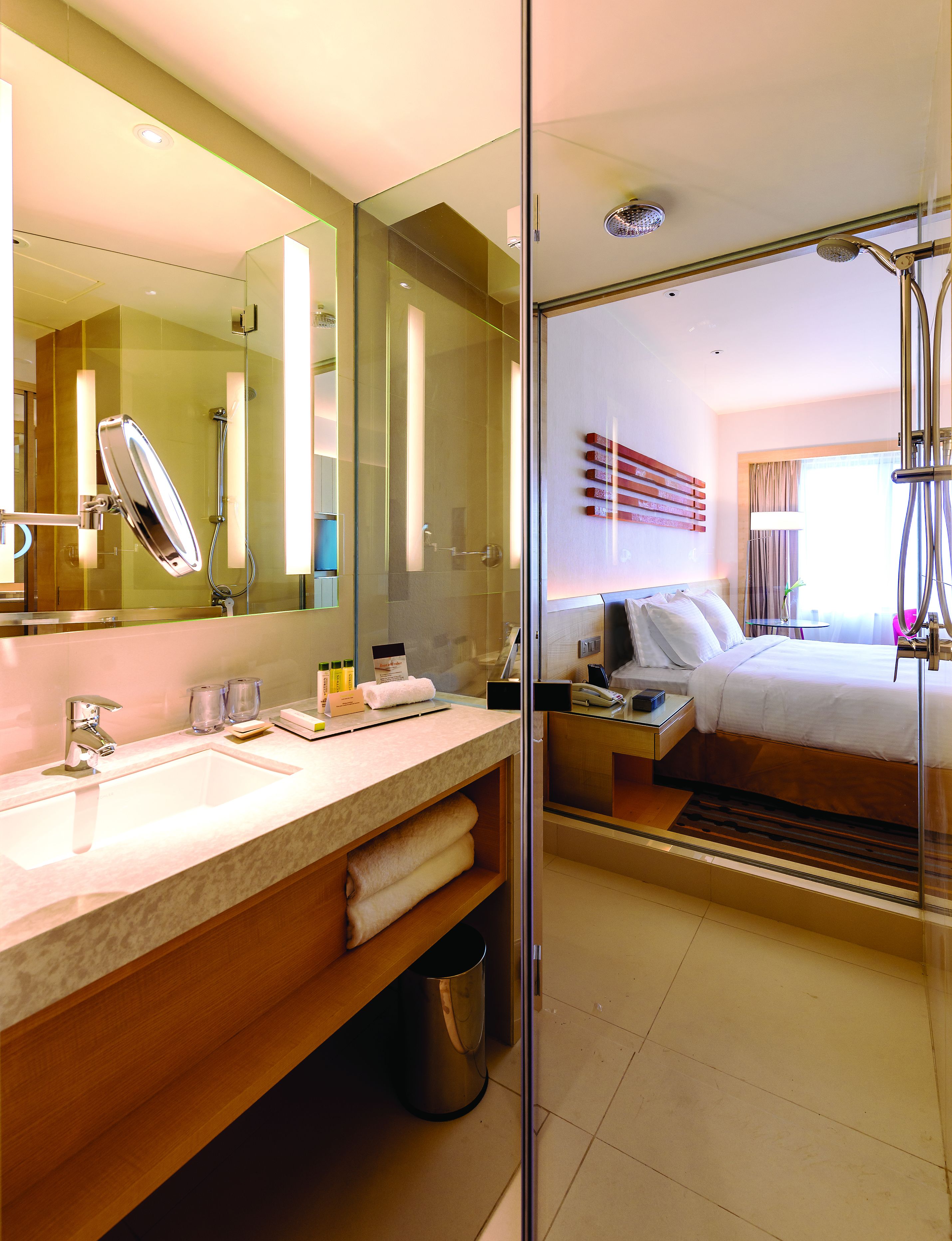 Un baño de hotel moderno con cabina de ducha de vidrio, un espejo grande y una zona de lavamanos separada.