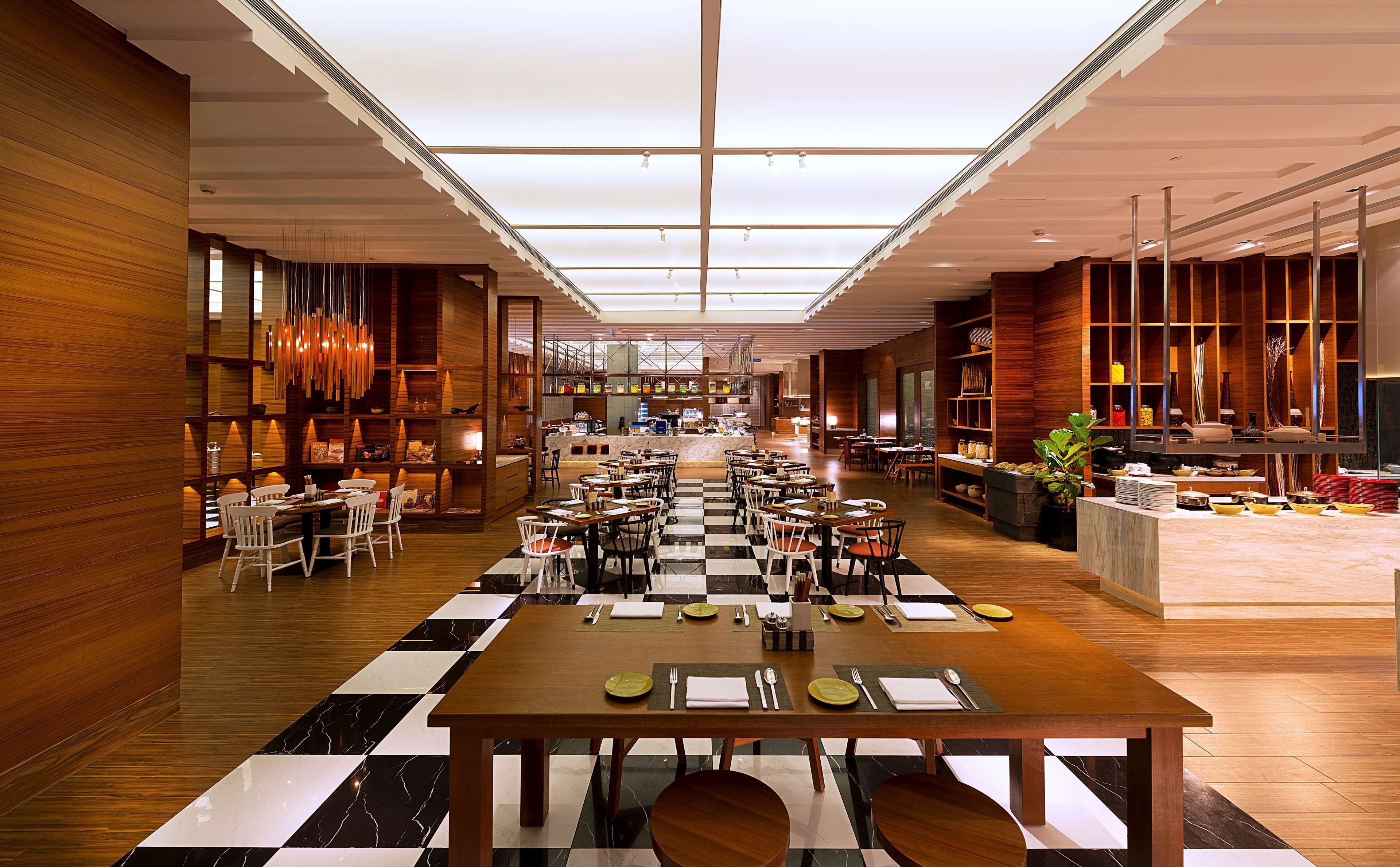 A spacious hotel lobby with a checkered floor, wooden paneling, and a central seating area with tables and chairs.