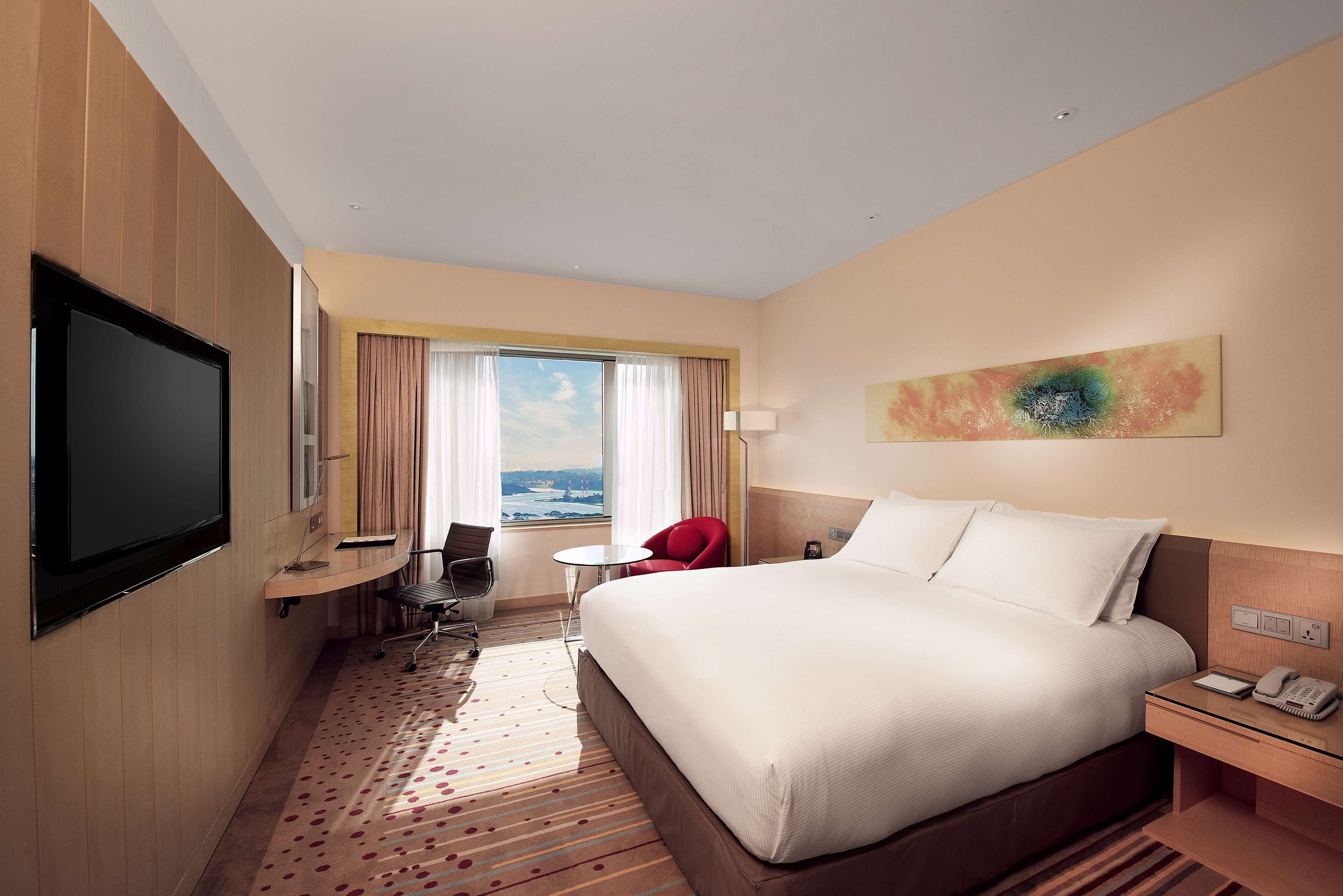 A hotel room with a large bed, a desk with a chair, a television, and a view of the city through the window.