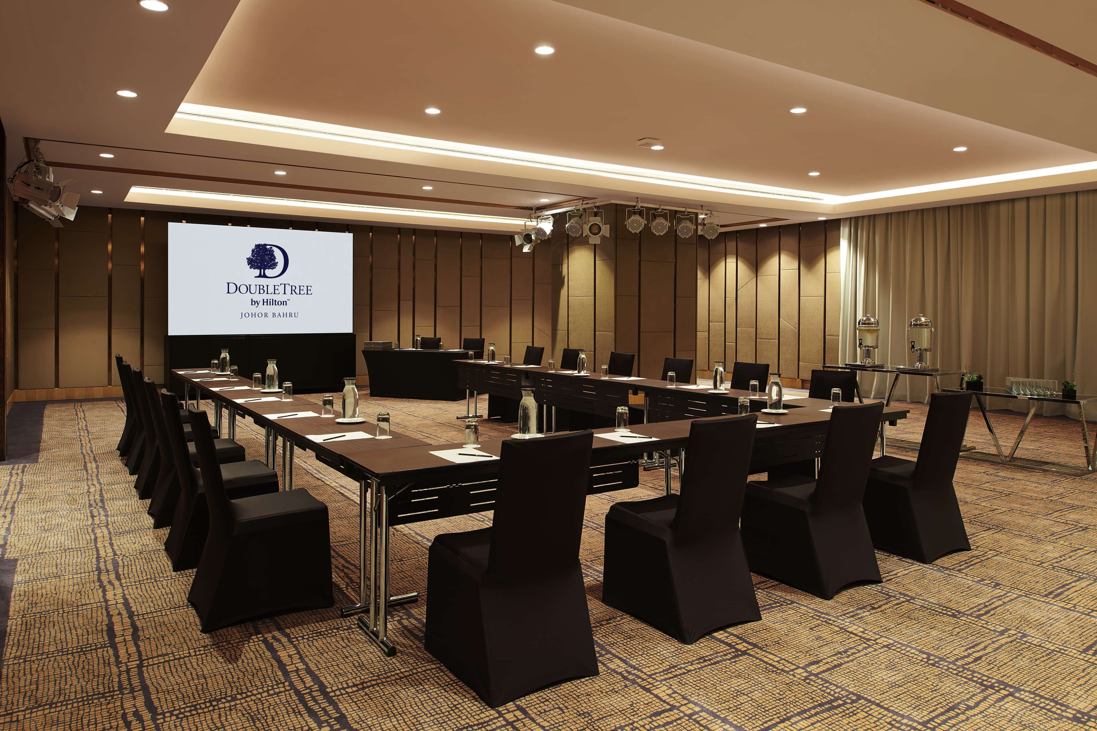 Un salón de conferencias con una larga mesa, sillas y una pantalla proyectora que muestra el logotipo de DoubleTree.