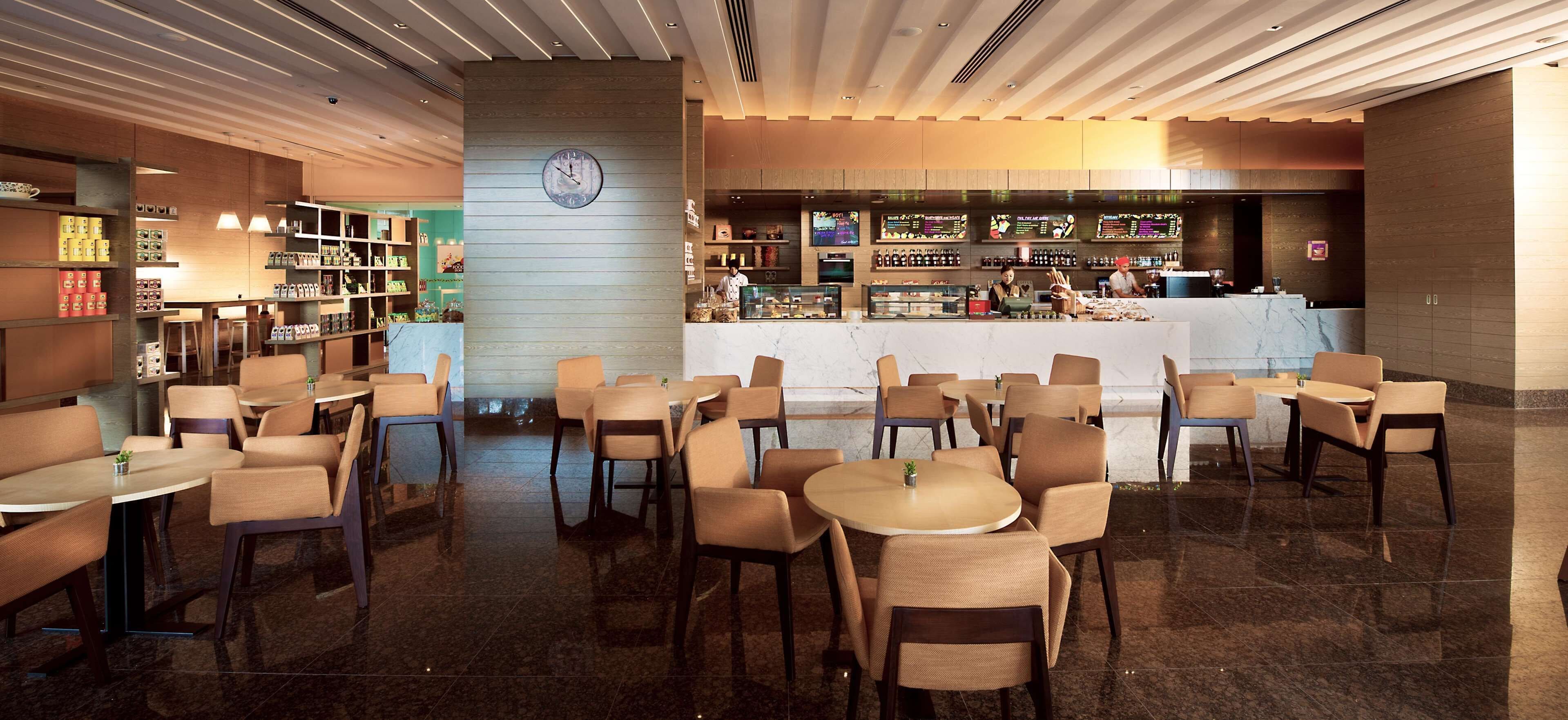 A modern cafe with multiple seating areas, a central bar, and a clock on the wall.