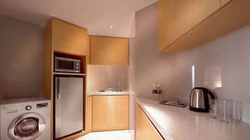 A compact kitchen with a washing machine, a microwave, a refrigerator, a sink, and a coffee maker.