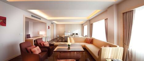 A modern hotel room with a living area, sofa, armchairs, a glass coffee table, and a dining area in the background.
