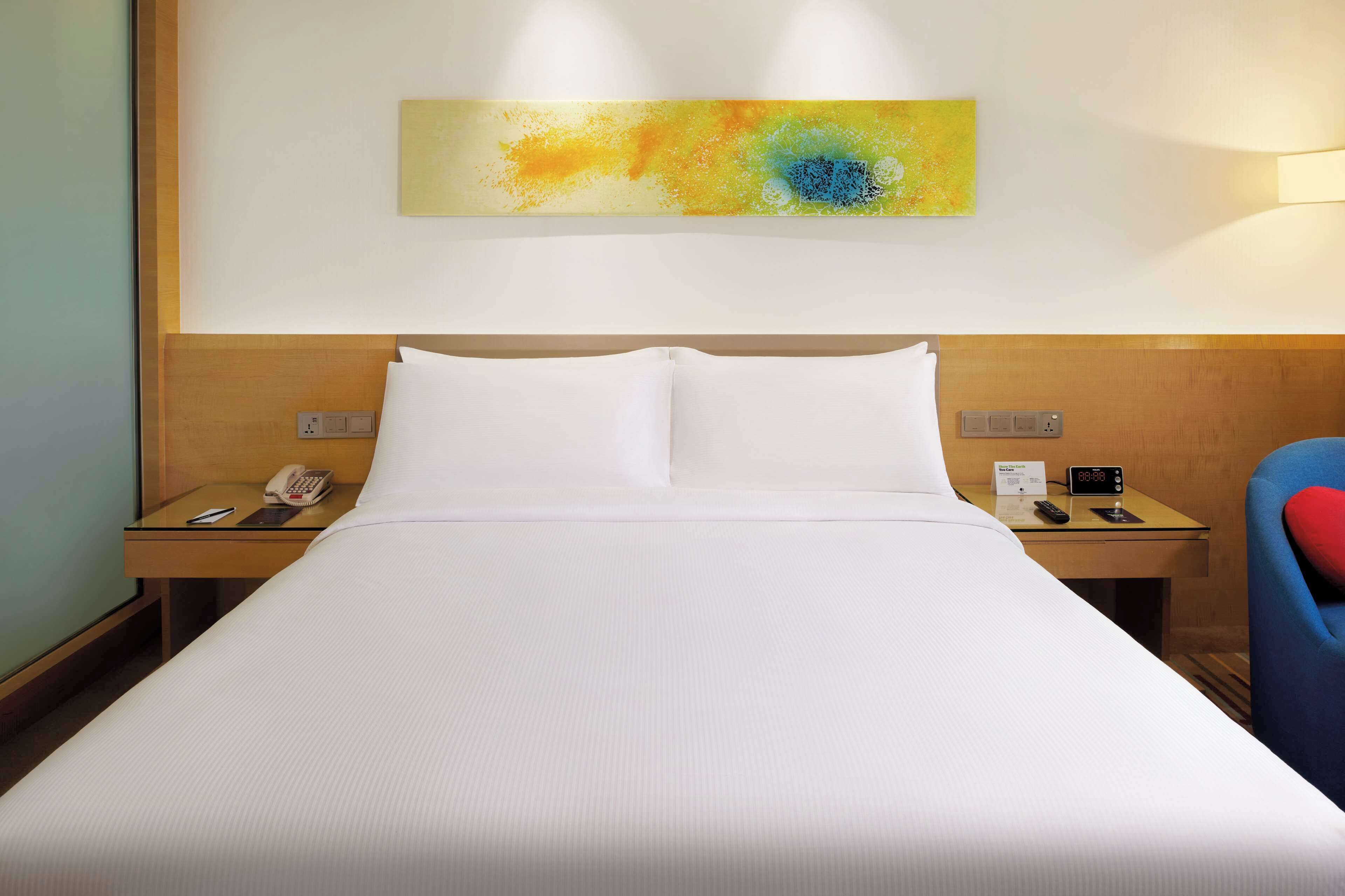 Une chambre d’hôtel avec un grand lit, deux tables de chevet, un téléphone, une horloge et une œuvre d’art murale.