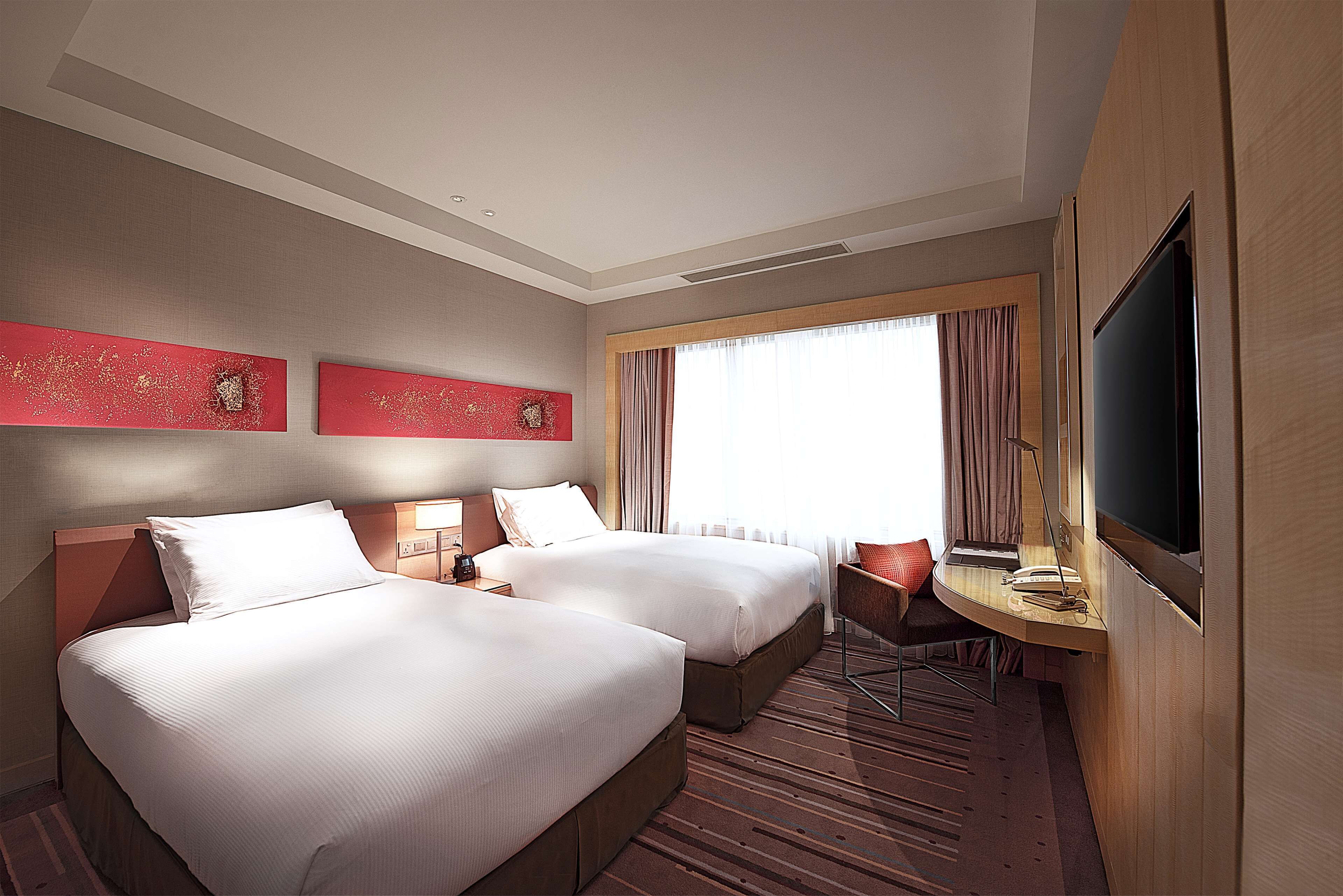 A hotel room with two beds, a desk with a chair, a television, and artwork on the wall.