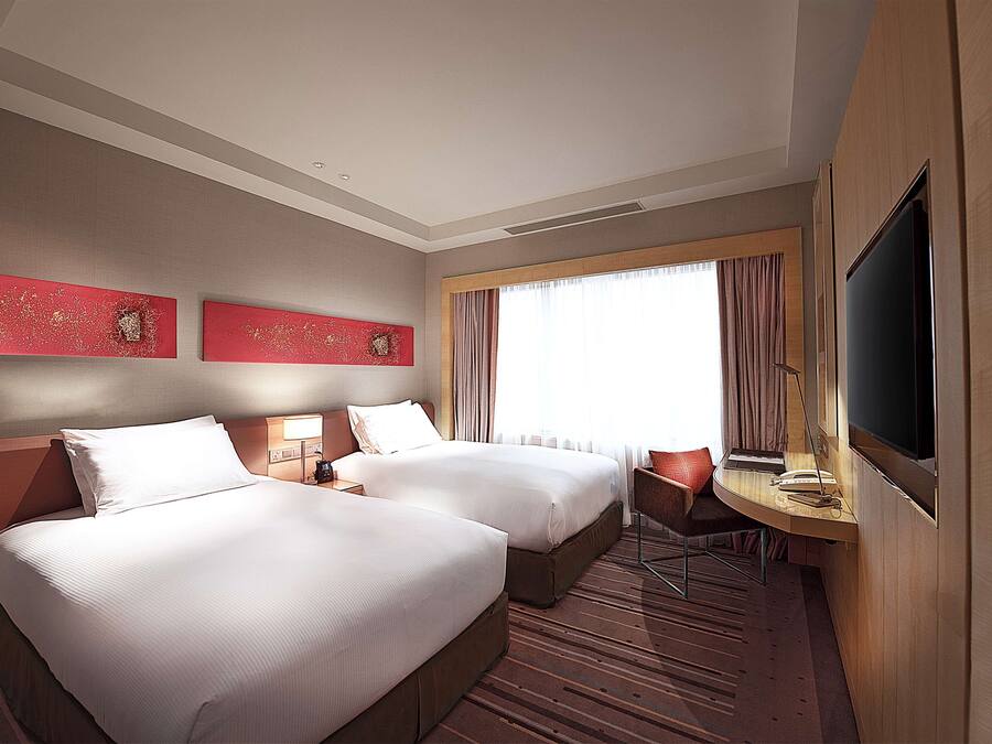 A hotel room with two beds, a desk with a chair, a television, and artwork on the wall.