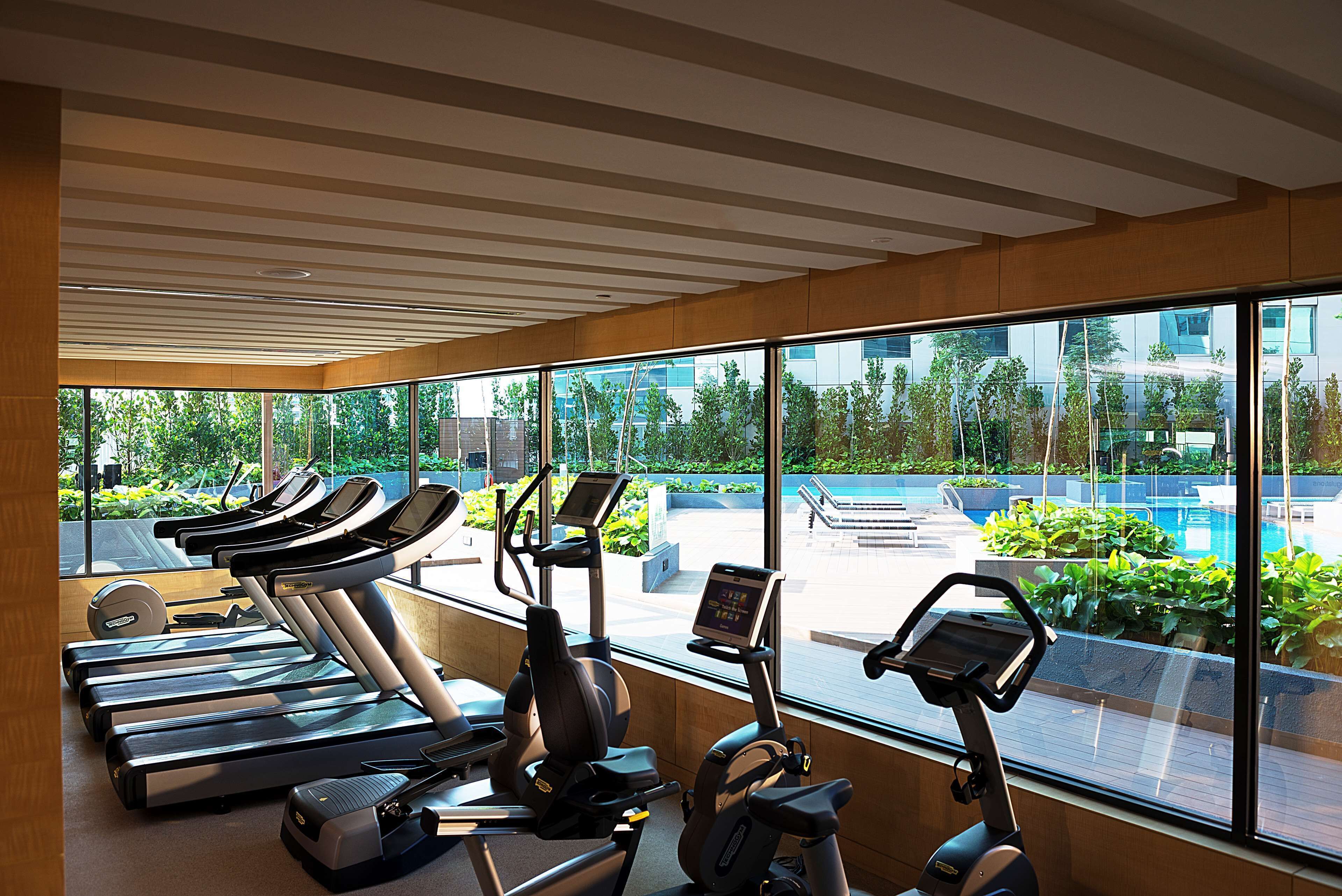 A gym with treadmills and stationary bikes, large windows with a view of a swimming pool and greenery.