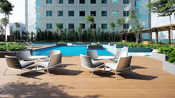 Área de piscina no terraço com espreguiçadeiras e vista para um edifício moderno.