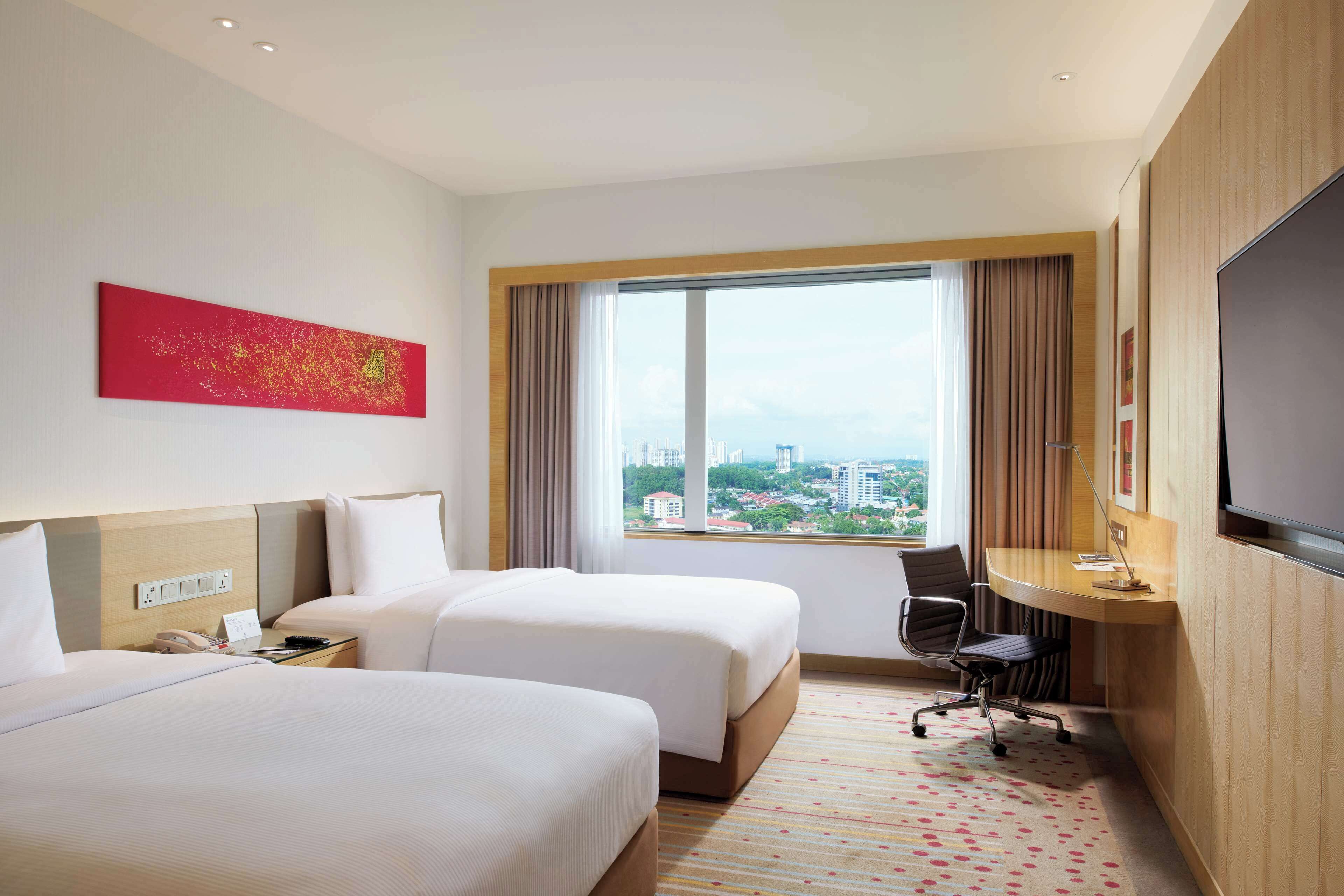 Habitación de hotel con dos camas, un escritorio, una silla, un televisor y un ventanal con vistas a la ciudad.