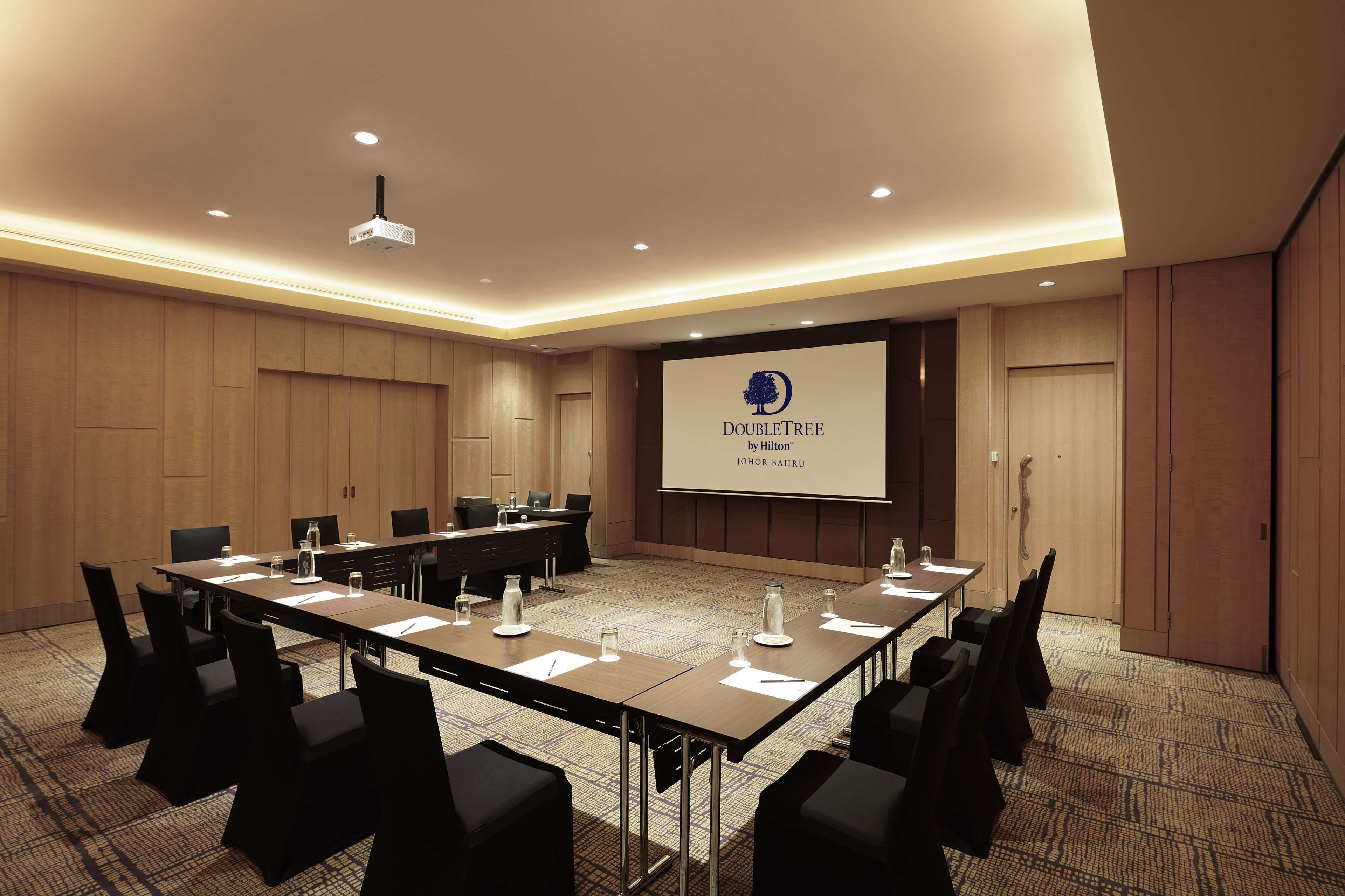 A conference room with a long table, chairs, a projector screen, and a presentation on the wall.