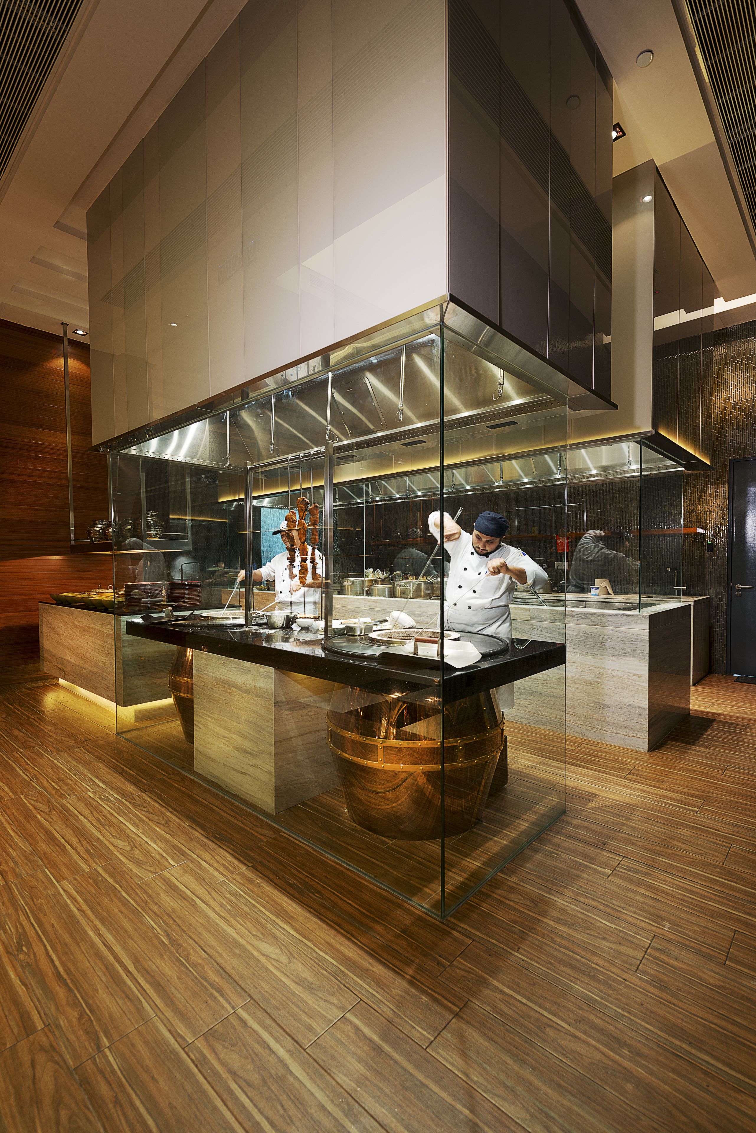 A modern kitchen with a chef preparing food, a stainless steel counter, and a large glass enclosure.