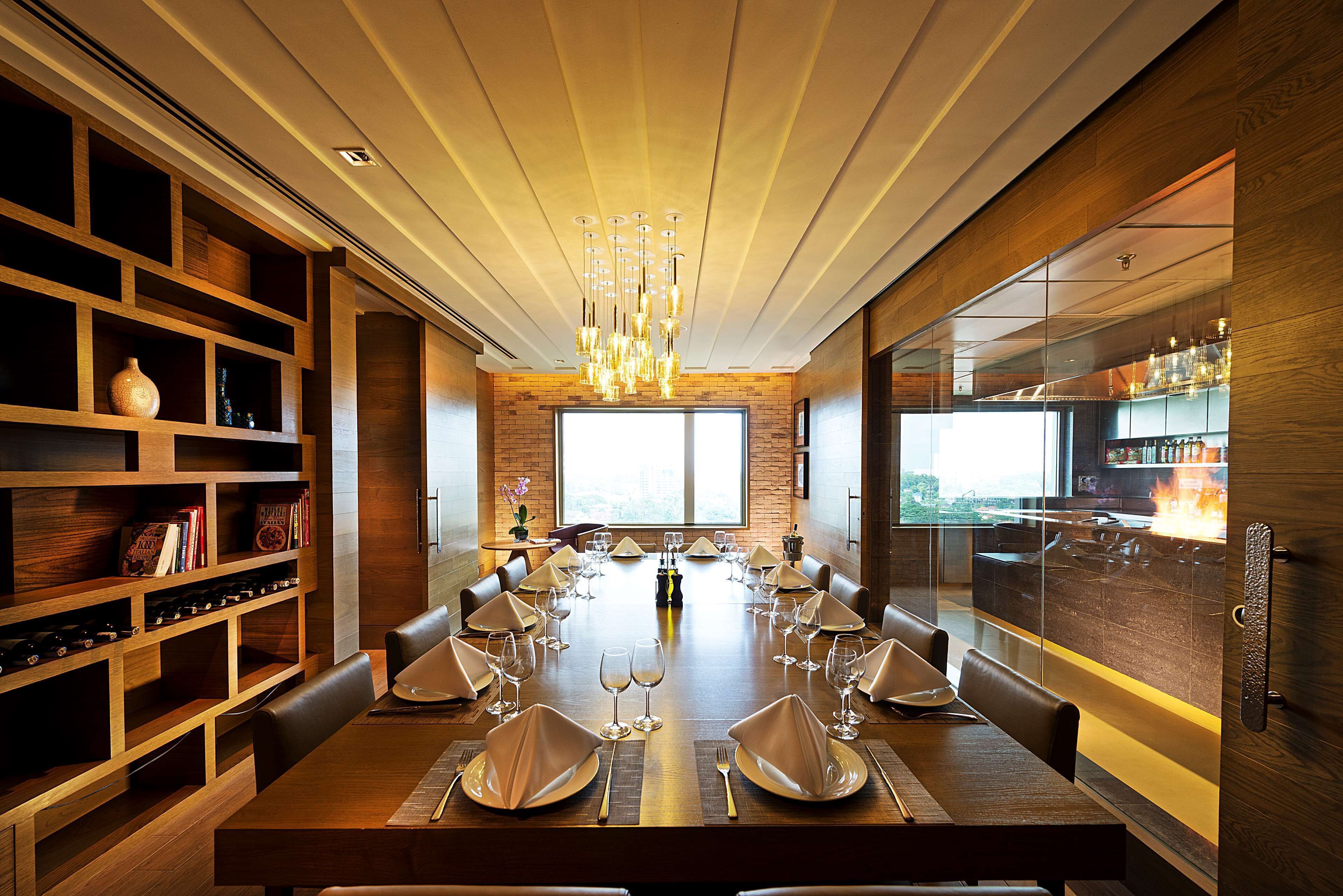 A modern dining room with a long table set for a meal, wooden shelving, and a large window.