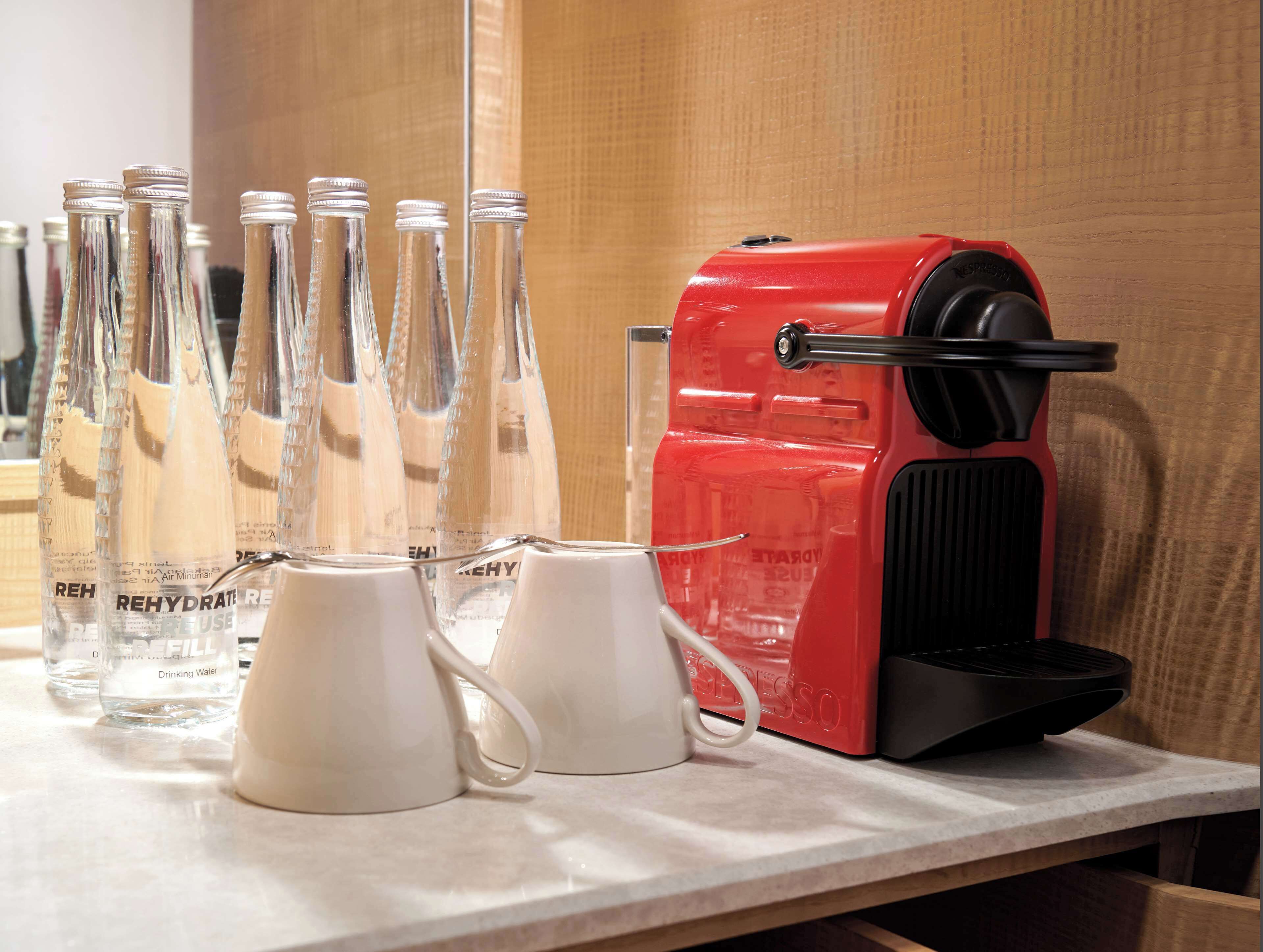 A kitchen counter with a red coffee maker, several clear glass bottles, and white mugs.
