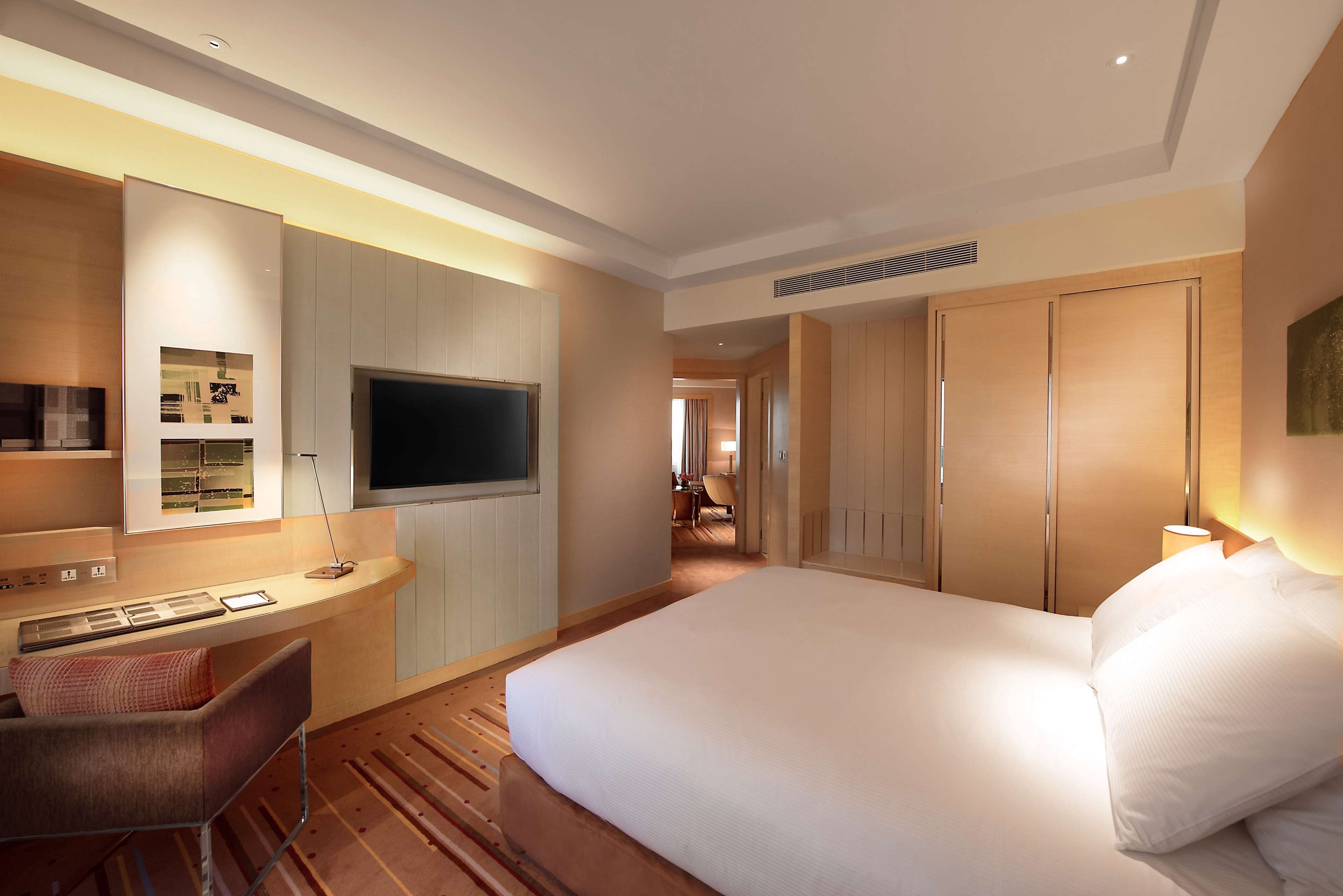 A hotel room with a large bed, a desk with a chair, a TV, and a wardrobe.