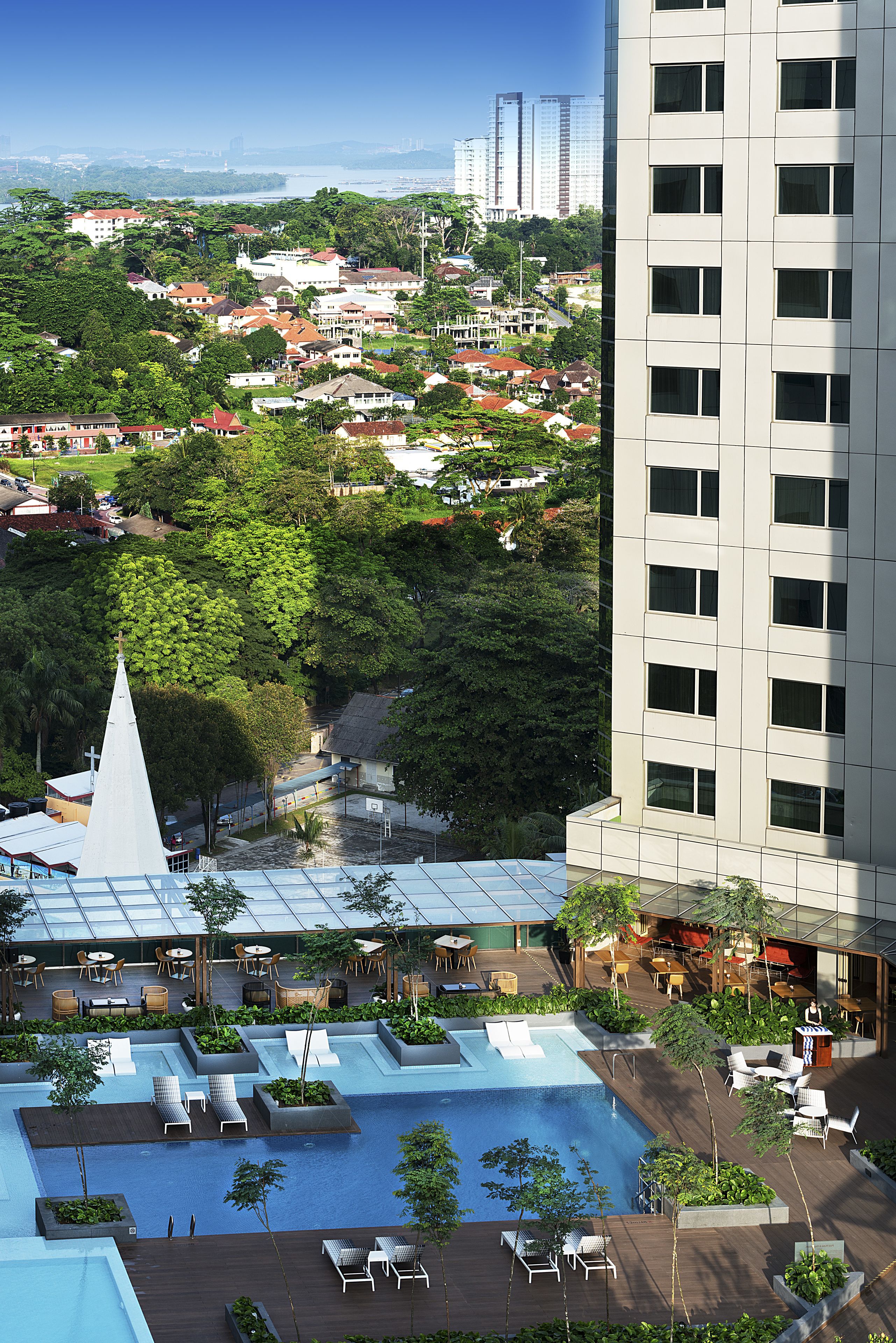 A hotel with a rooftop pool, lush greenery, and a view of the cityscape.