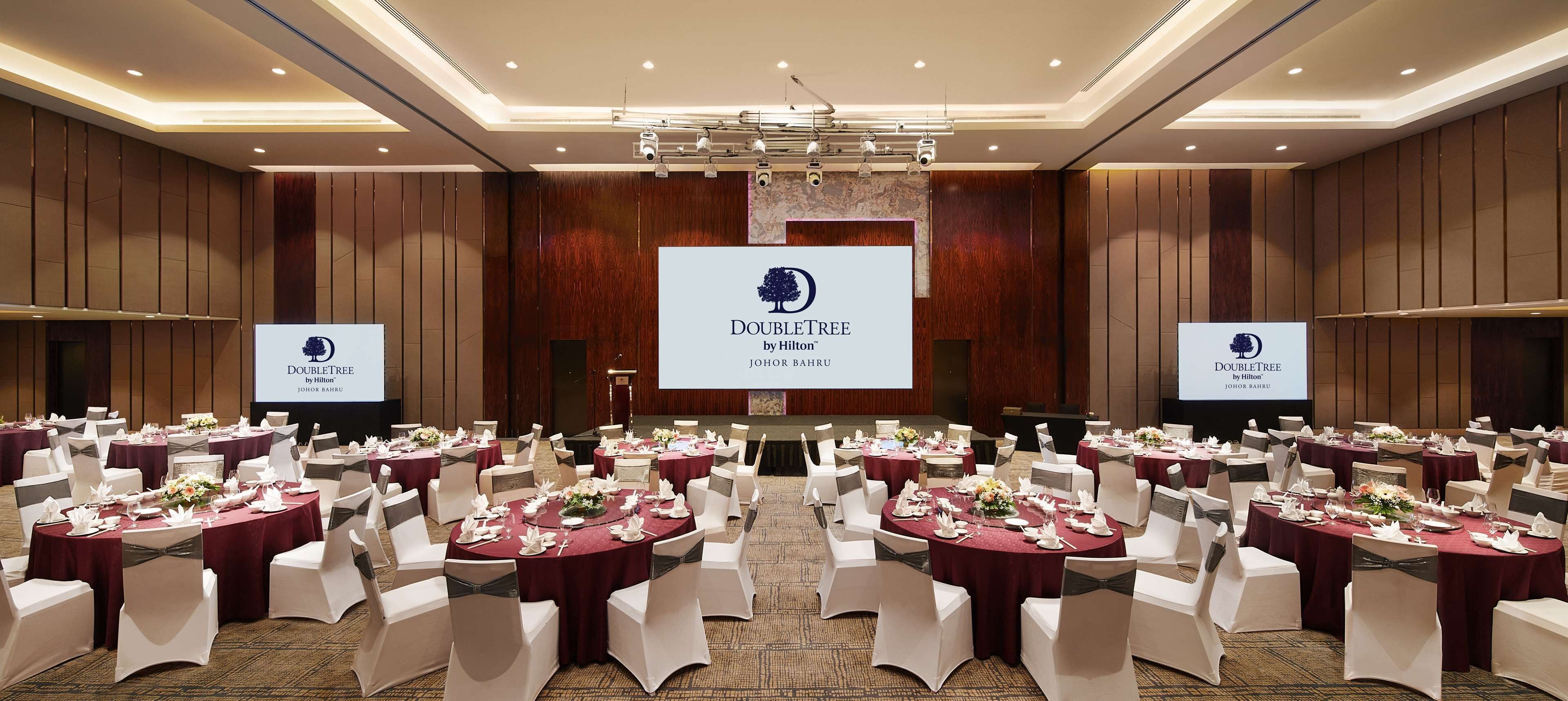 A conference room with round tables, white chairs, and a large screen displaying the DoubleTree logo.