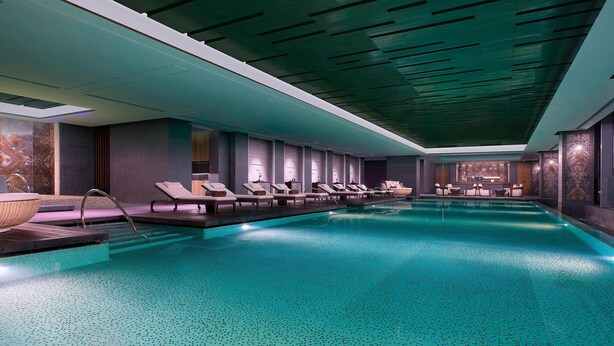 Une piscine intérieure moderne, dotée de chaises longues et d’un espace bar.