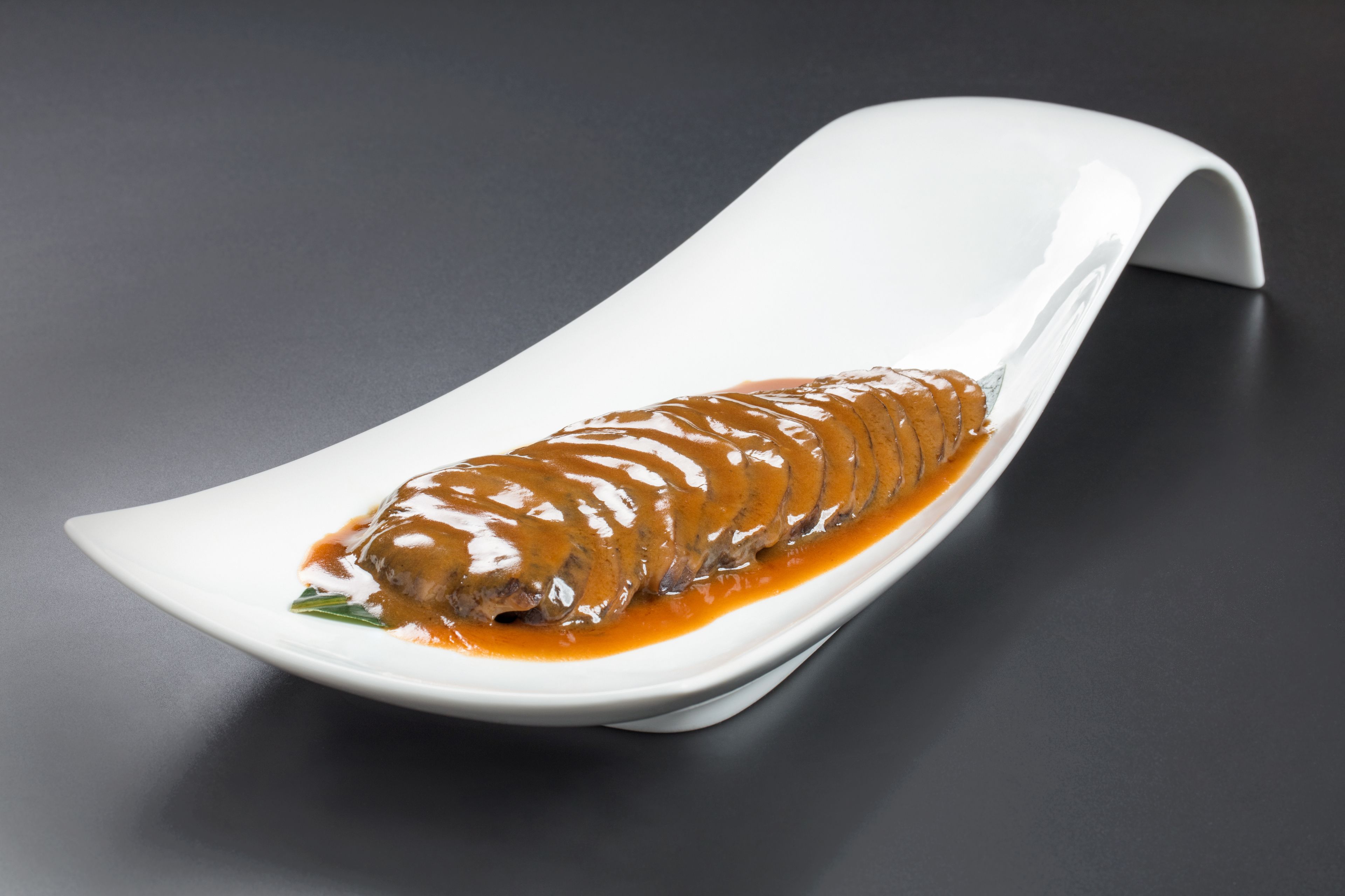 A white plate with a rolled meat dish and sauce on a dark surface.