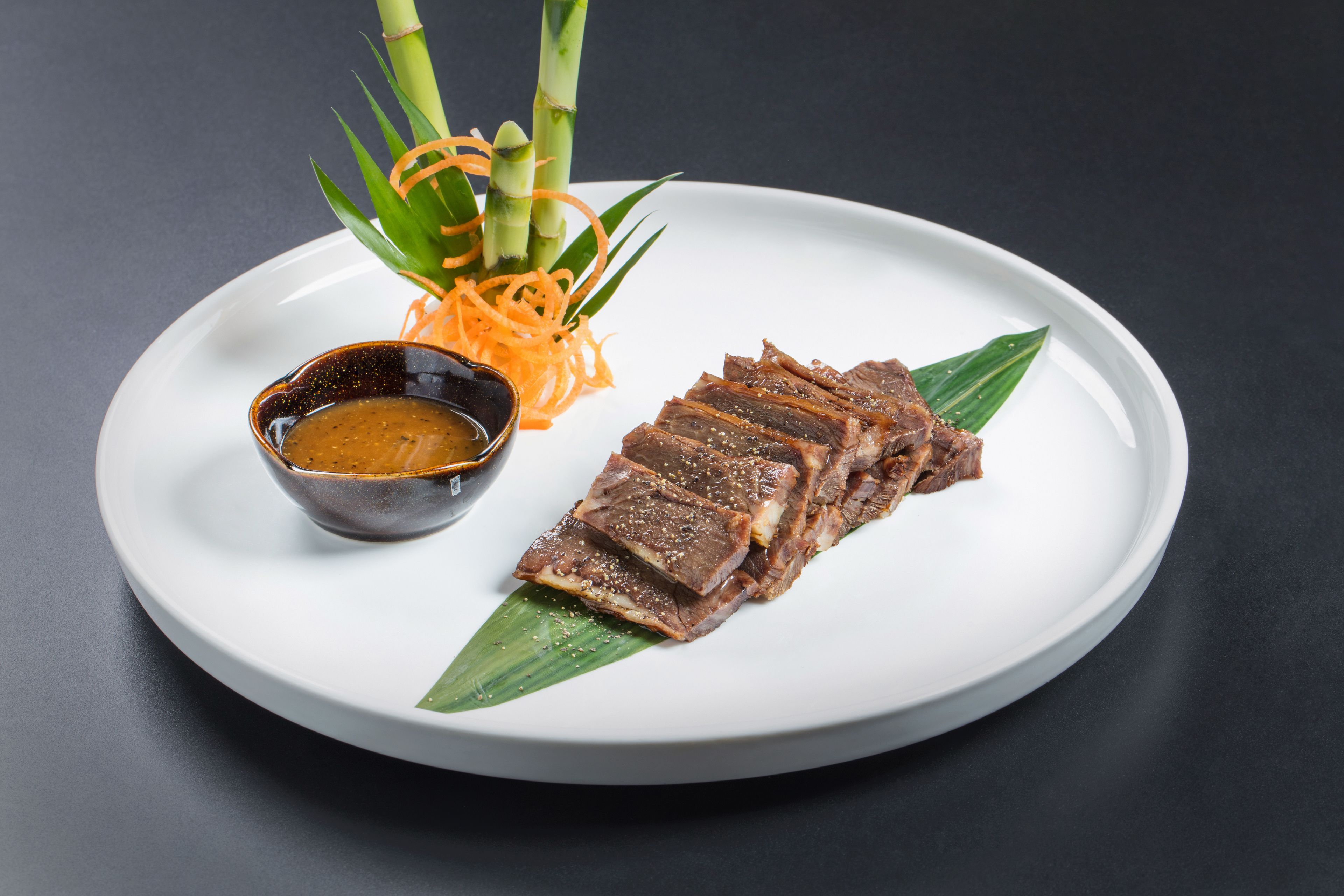 Un plato con carne en rodajas, un recipiente pequeño con salsa y una guarnición decorativa.